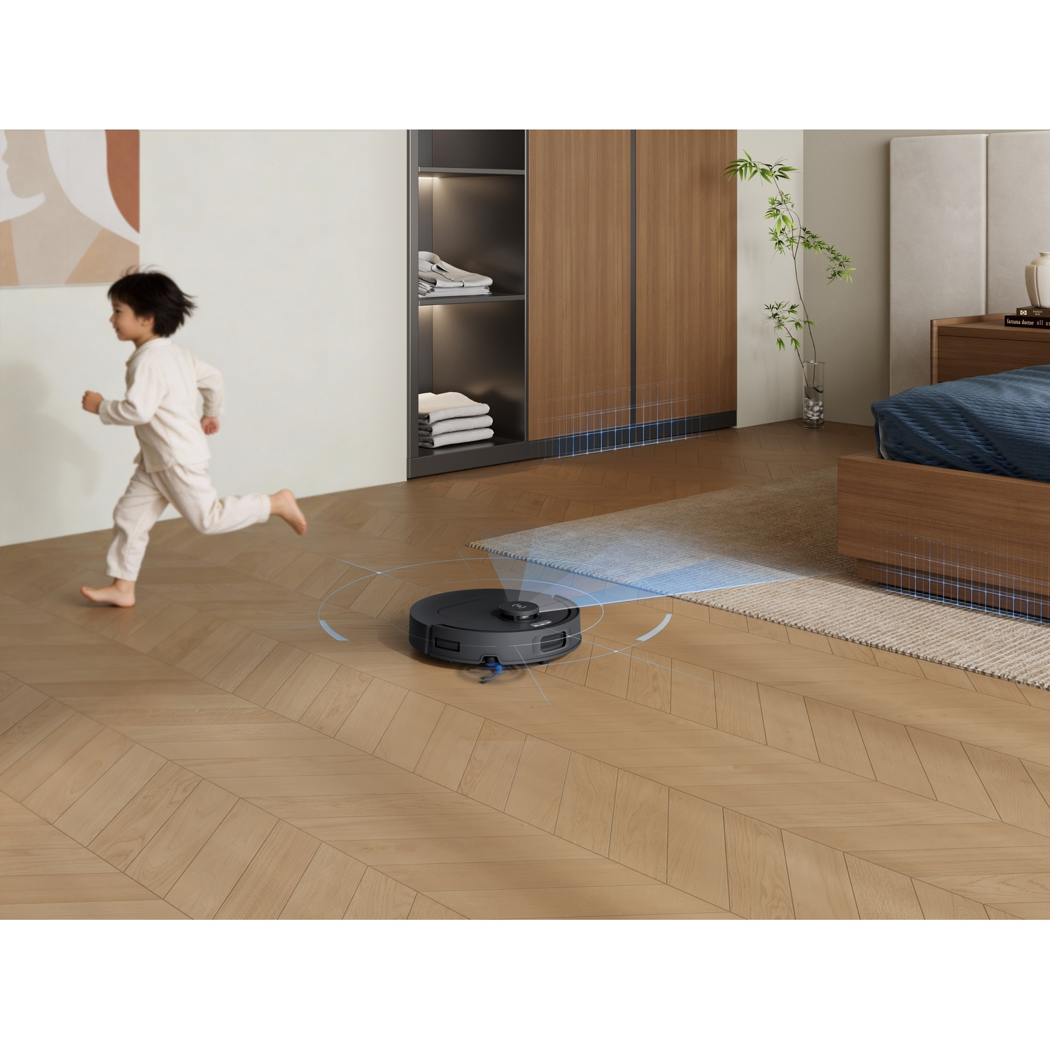 Un bambino in pigiama corre su un pavimento in legno mentre un robot aspirapolvere pulisce.