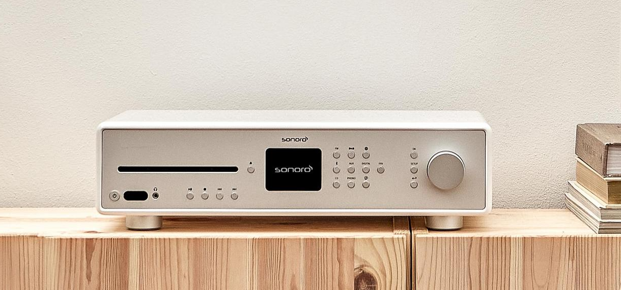 Ein silbernes Hi-Fi-Gerät mit CD-Schlitz, Display und Drehknopf auf einem Holzschrank.