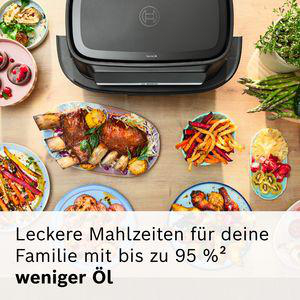 Ein Tisch voller Essen, darunter Rippchen, Pommes und Salat, vor einem Grill.