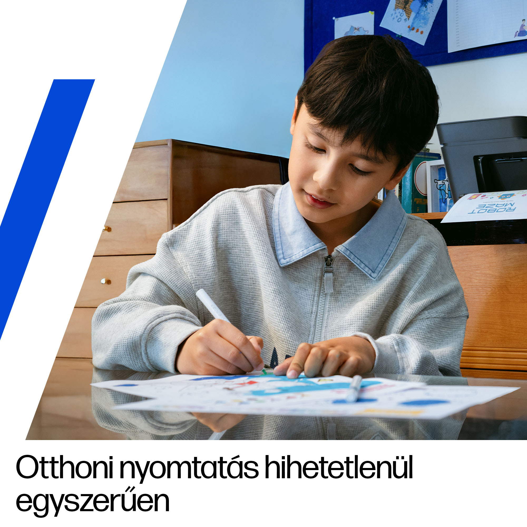 Egy fiú rajzol papírra ceruzákkal, mellette egy nyomtató.