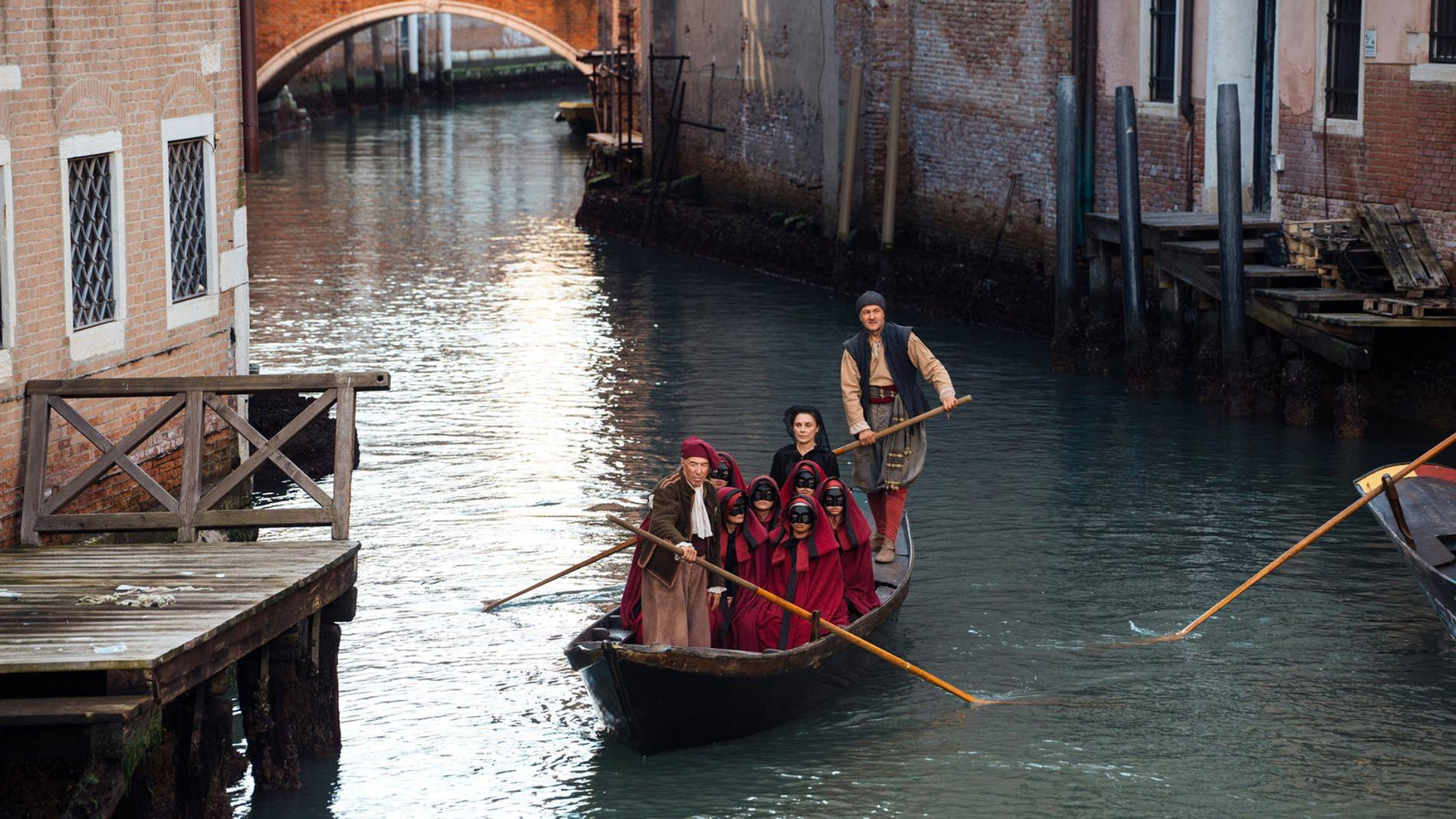Menschen in traditioneller Kleidung und Masken rudern in einem Boot durch einen Kanal in Venedig.