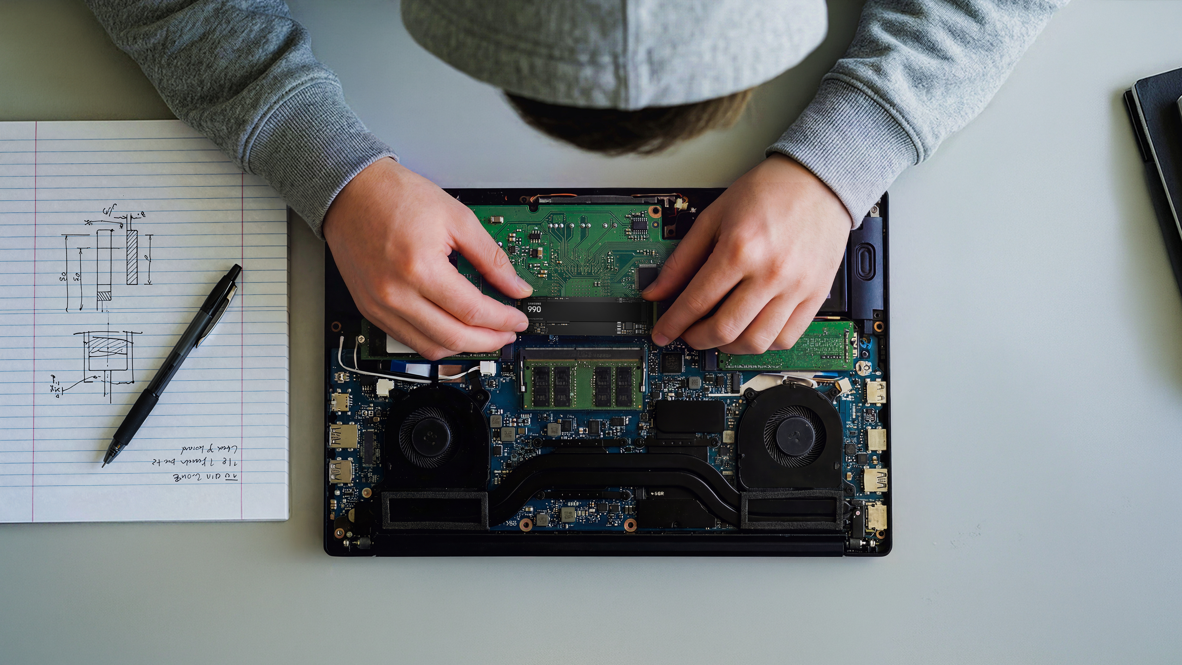 Person fügt eine SSD-Karte in ein geöffnetes Laptop-Motherboard ein.