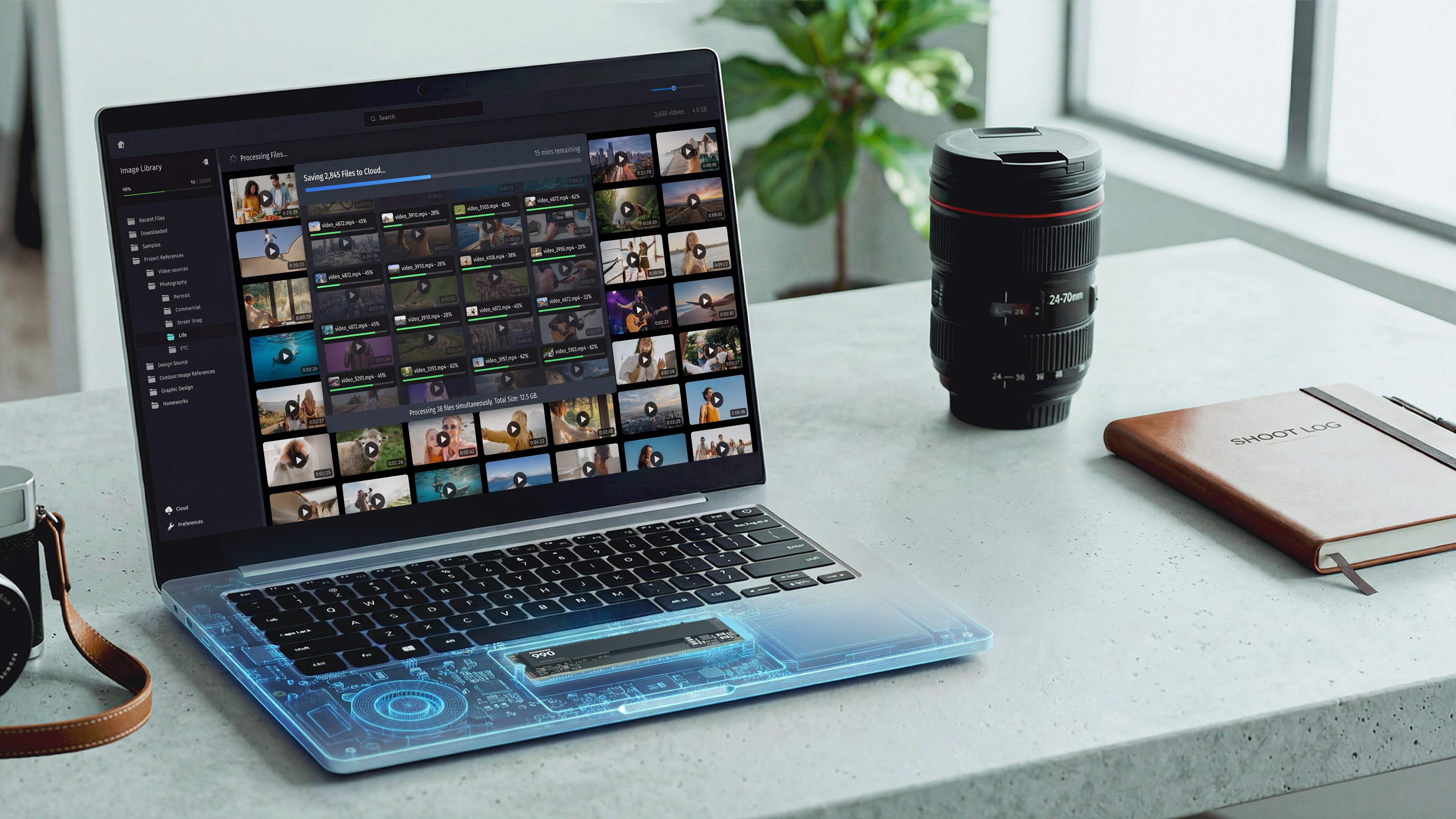 Laptop zeigt Videoverwaltung; Kameraobjektiv und Notizbuch daneben.
