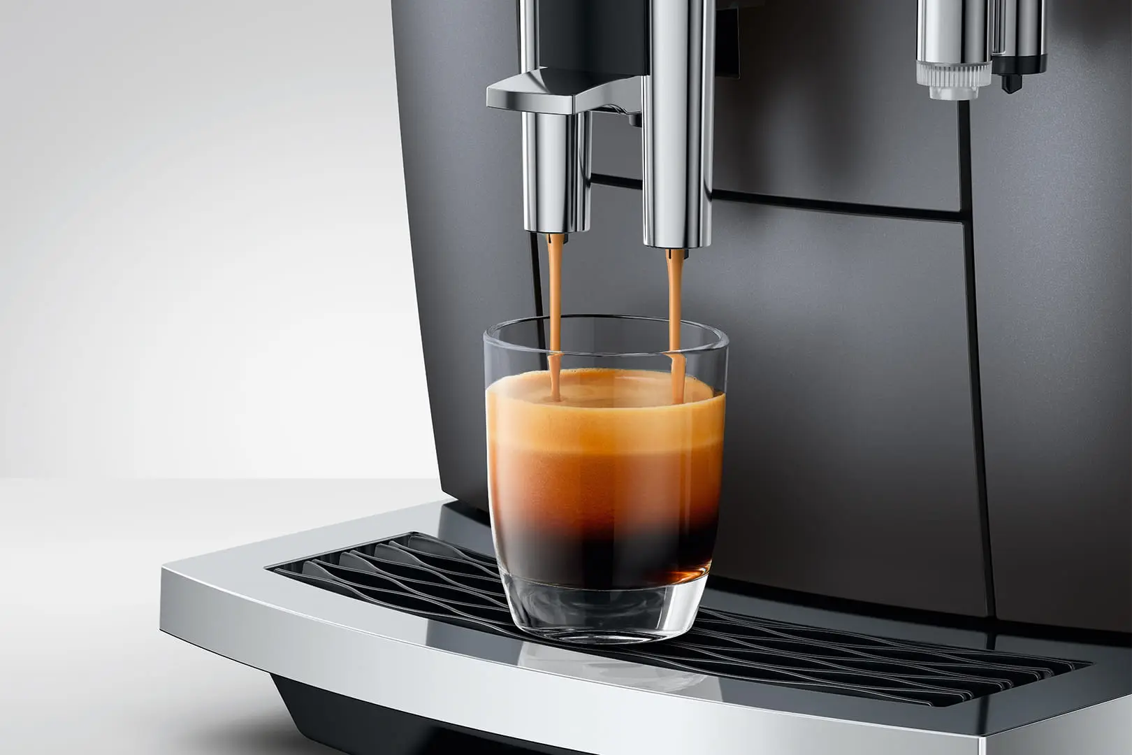 Macchina da caffè eroga espresso in un bicchiere su vassoio raccogligocce argentato.