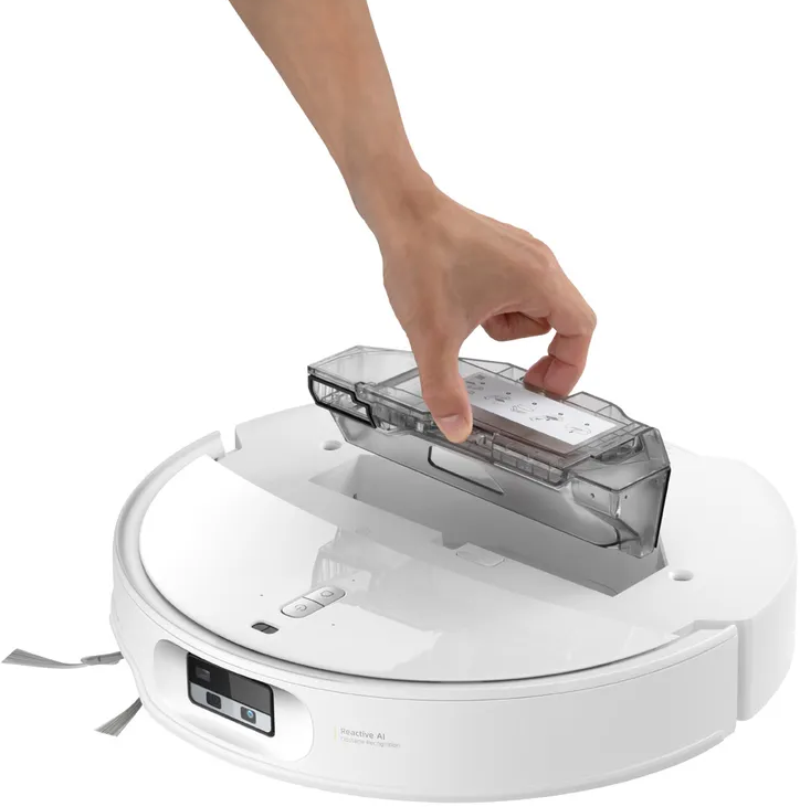 Une main insère un bac à poussière transparent dans un aspirateur robot blanc.