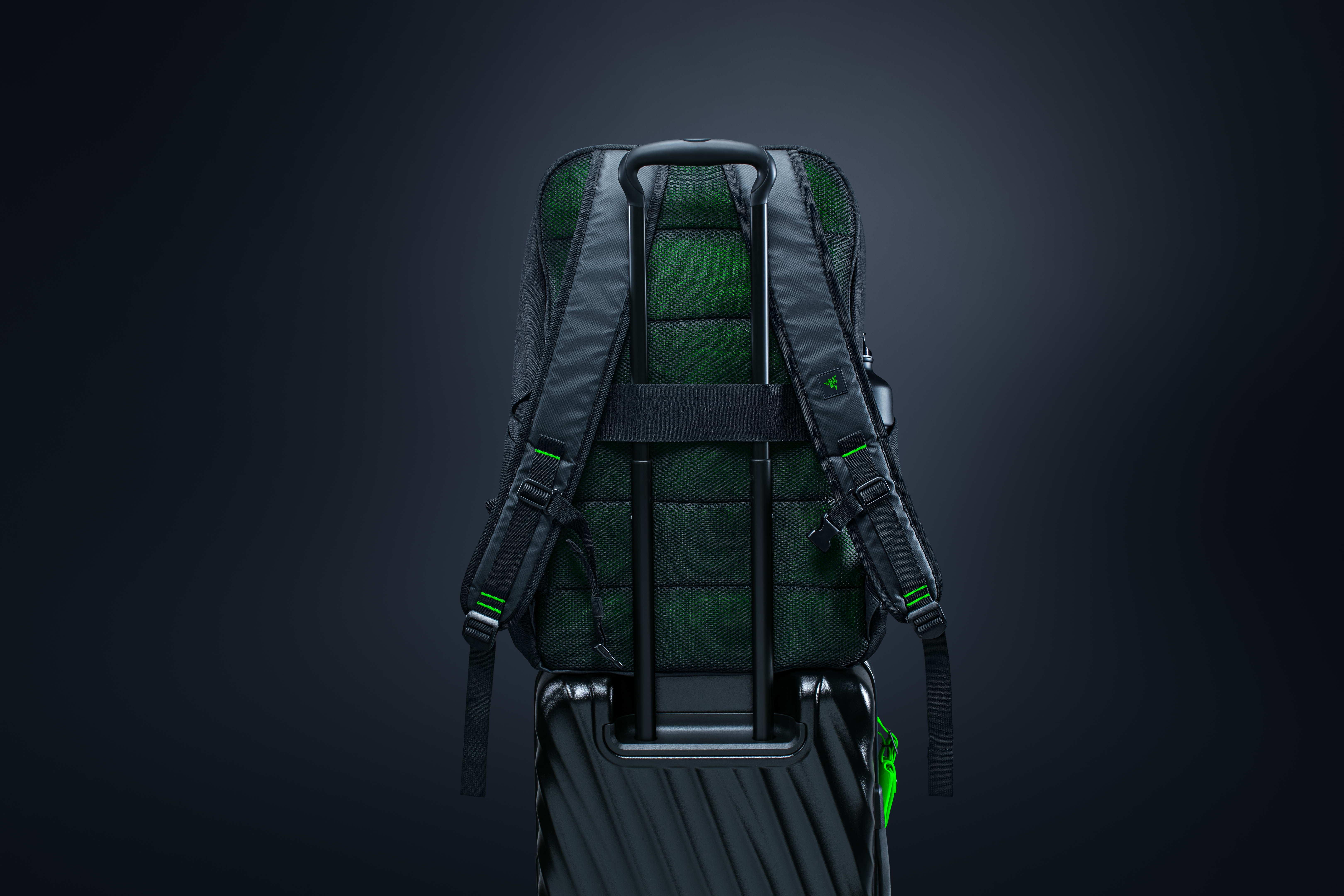 Schwarzer Rucksack mit grünen Akzenten auf schwarzem Koffer.