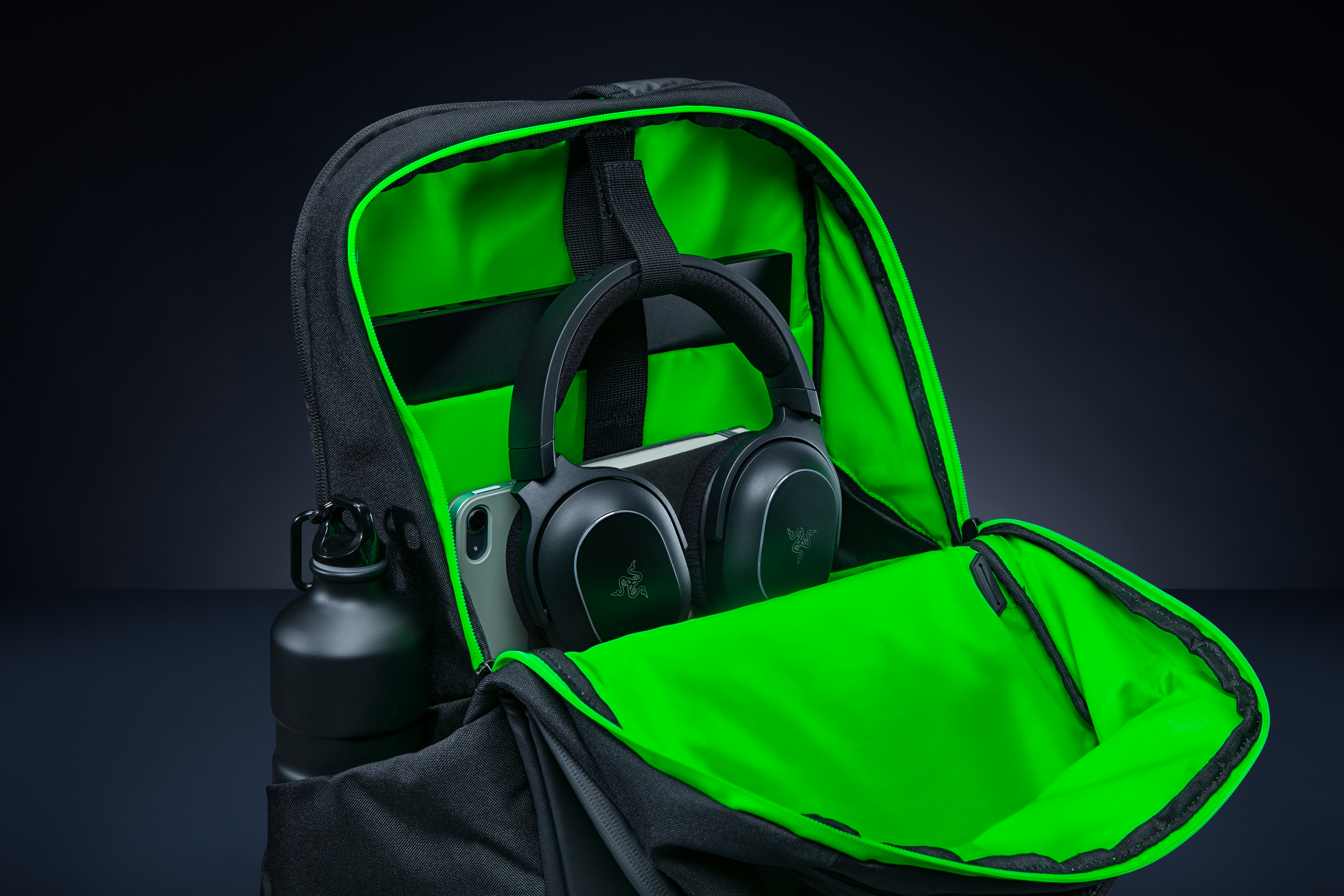 Offener schwarzer Rucksack mit leuchtend grüner Innenseite. Enthält Kopfhörer, Handy, Wasserflasche.