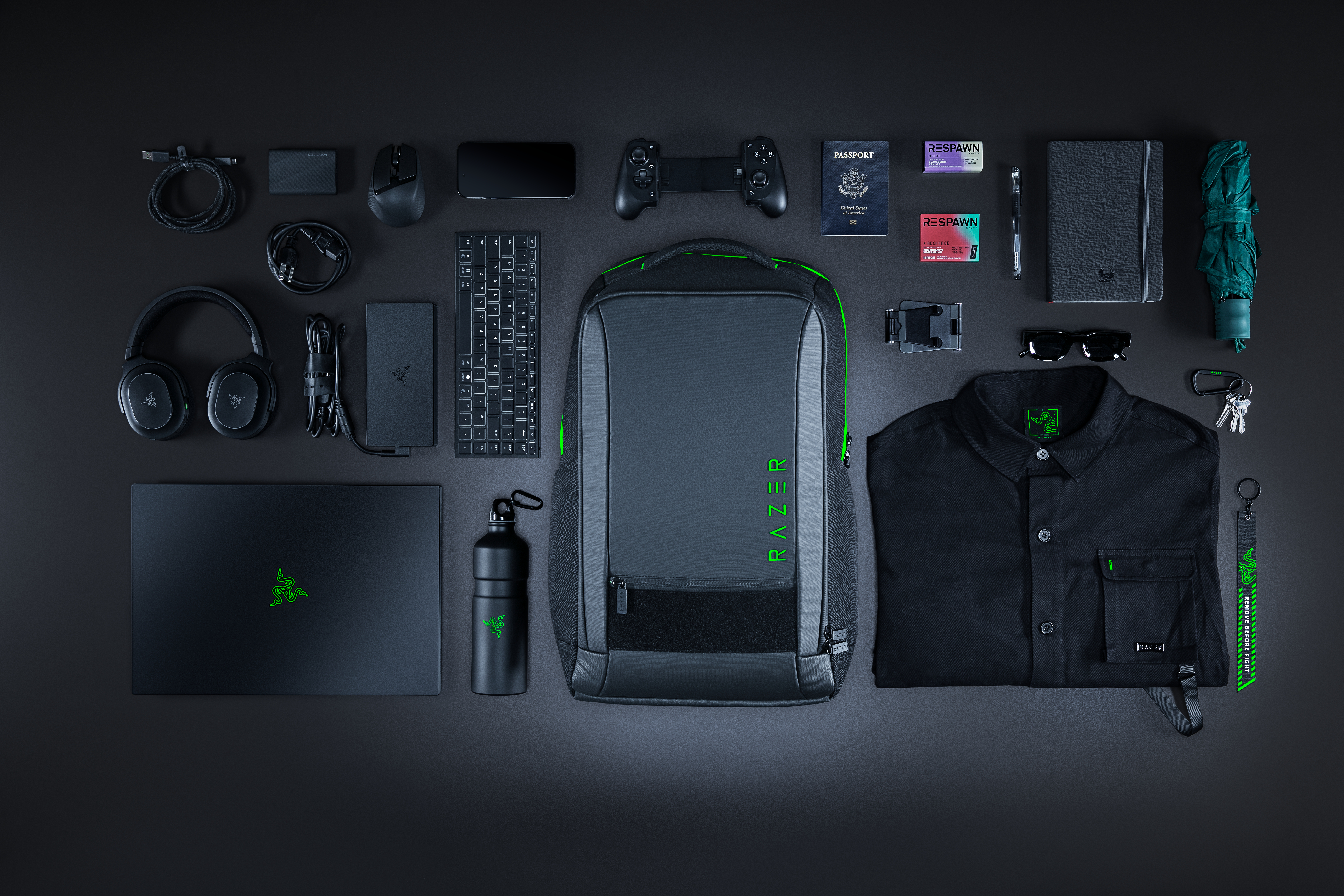 Schwarze Kleidung, Laptop, Kopfhörer, Tasche, Reisepass und Zubehör auf dunklem Hintergrund.