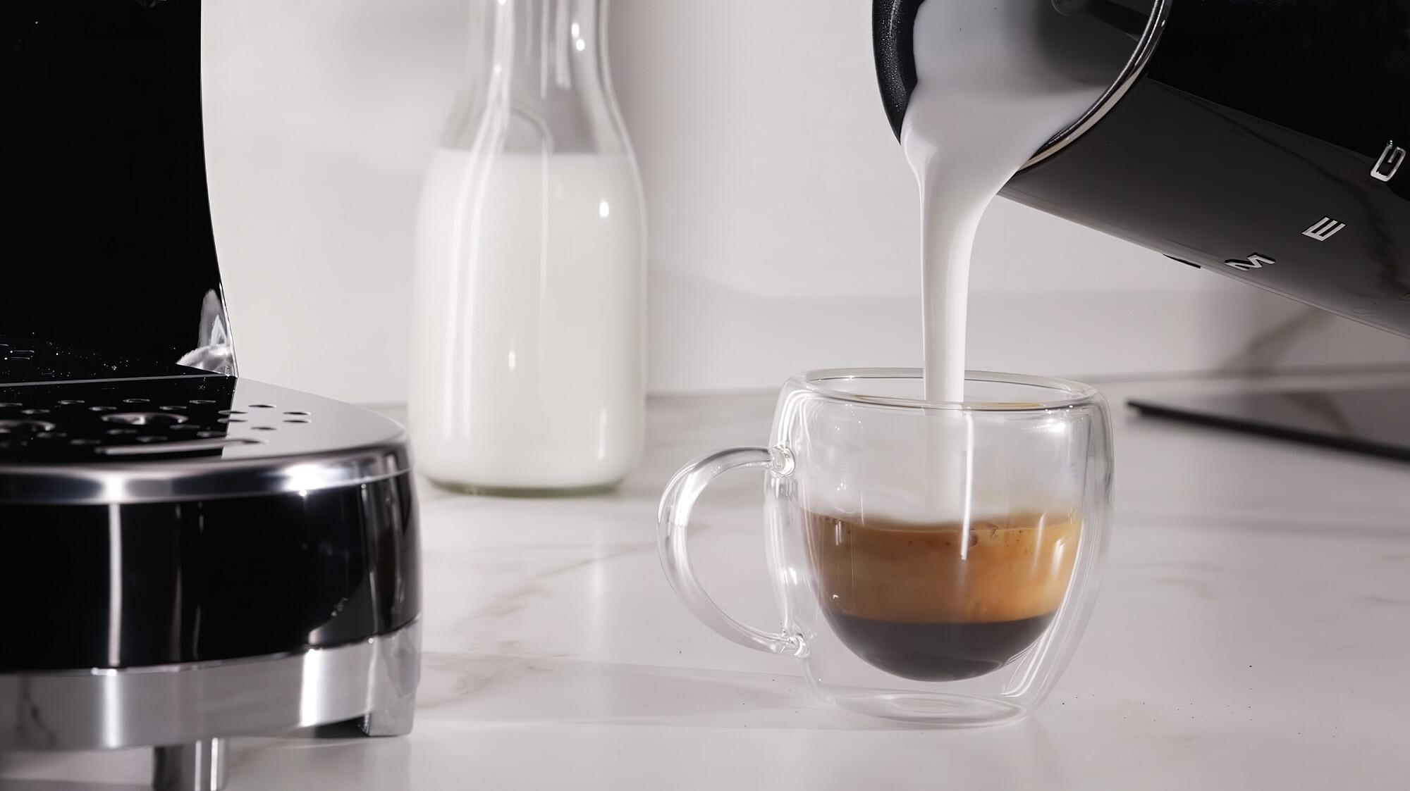 Milch wird in eine Espressotasse gegossen, daneben eine Milchflasche.