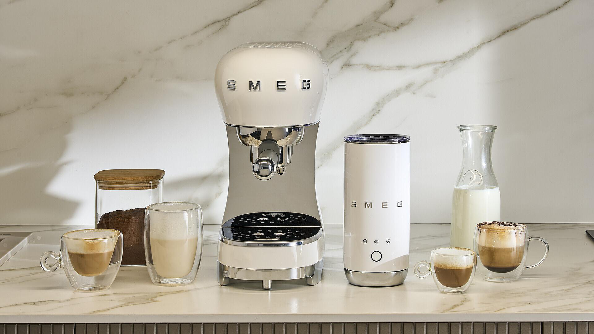 Weiße Smeg-Kaffeemaschine mit Zubehör: Kaffeebohnen, Milch und fertige Kaffees.