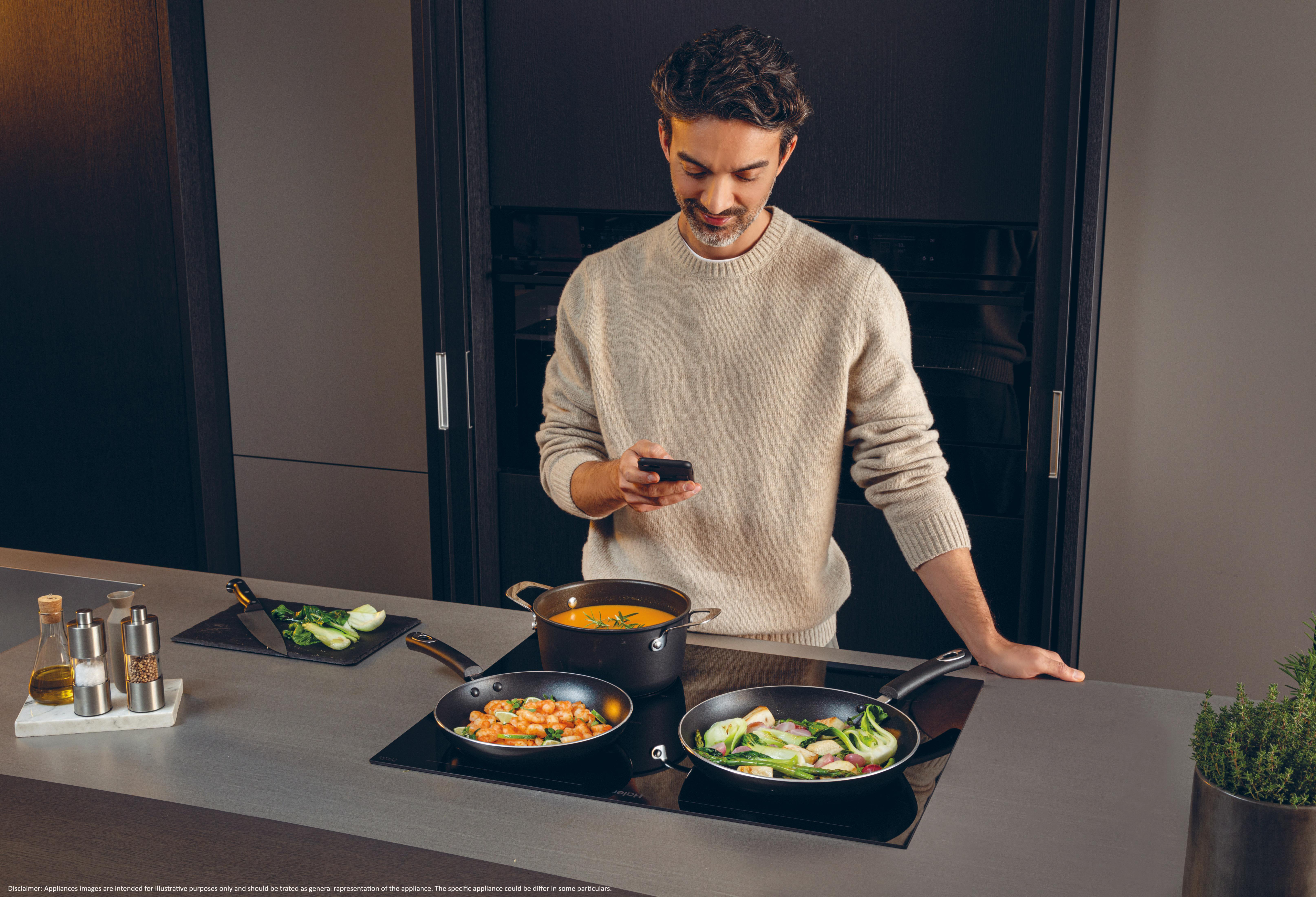 Ein Mann mit Handy kocht Garnelen und Gemüse in einer modernen Küche.