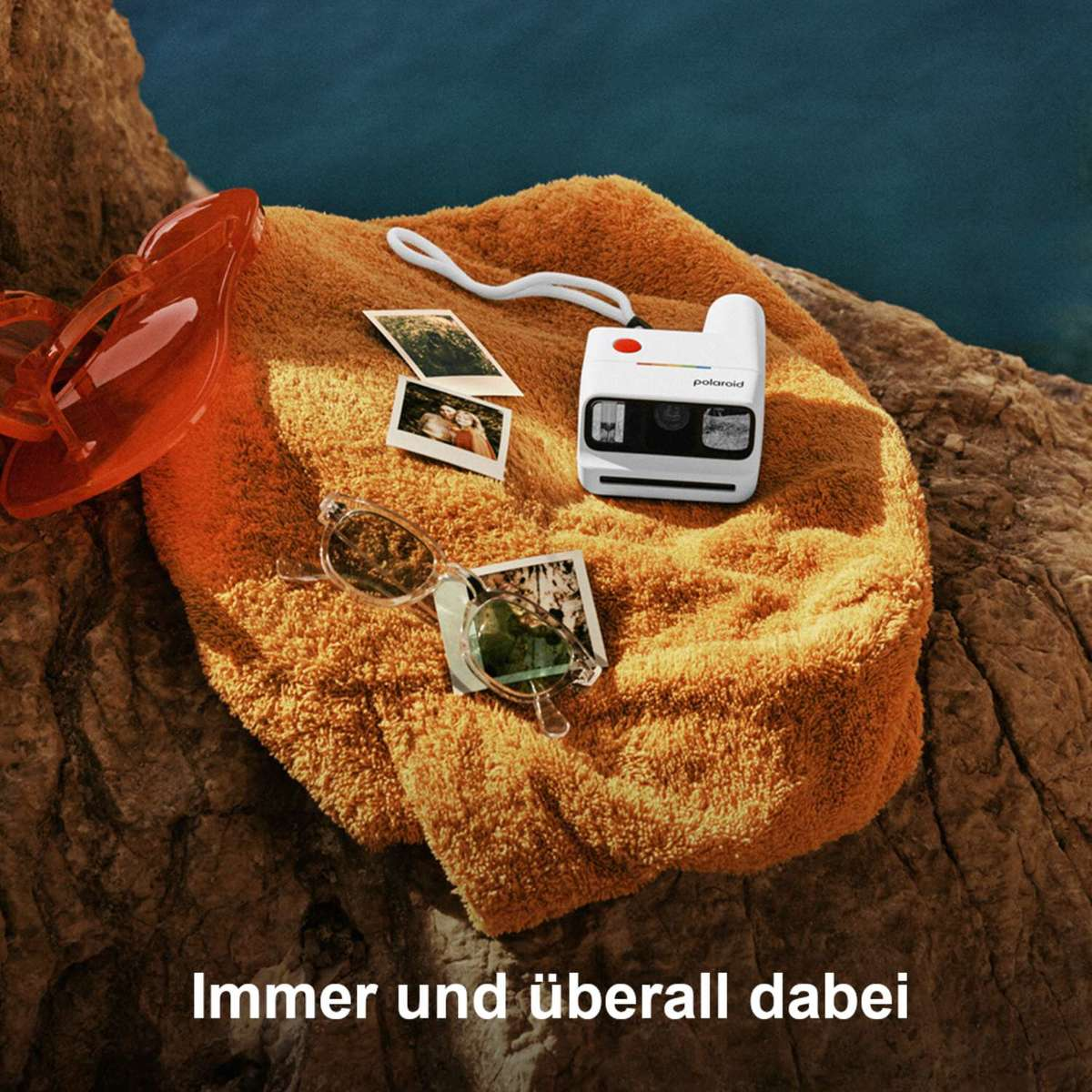 Orange Handtuch mit Polaroid Kamera, Sonnenbrille, Flip-Flops und Fotos.