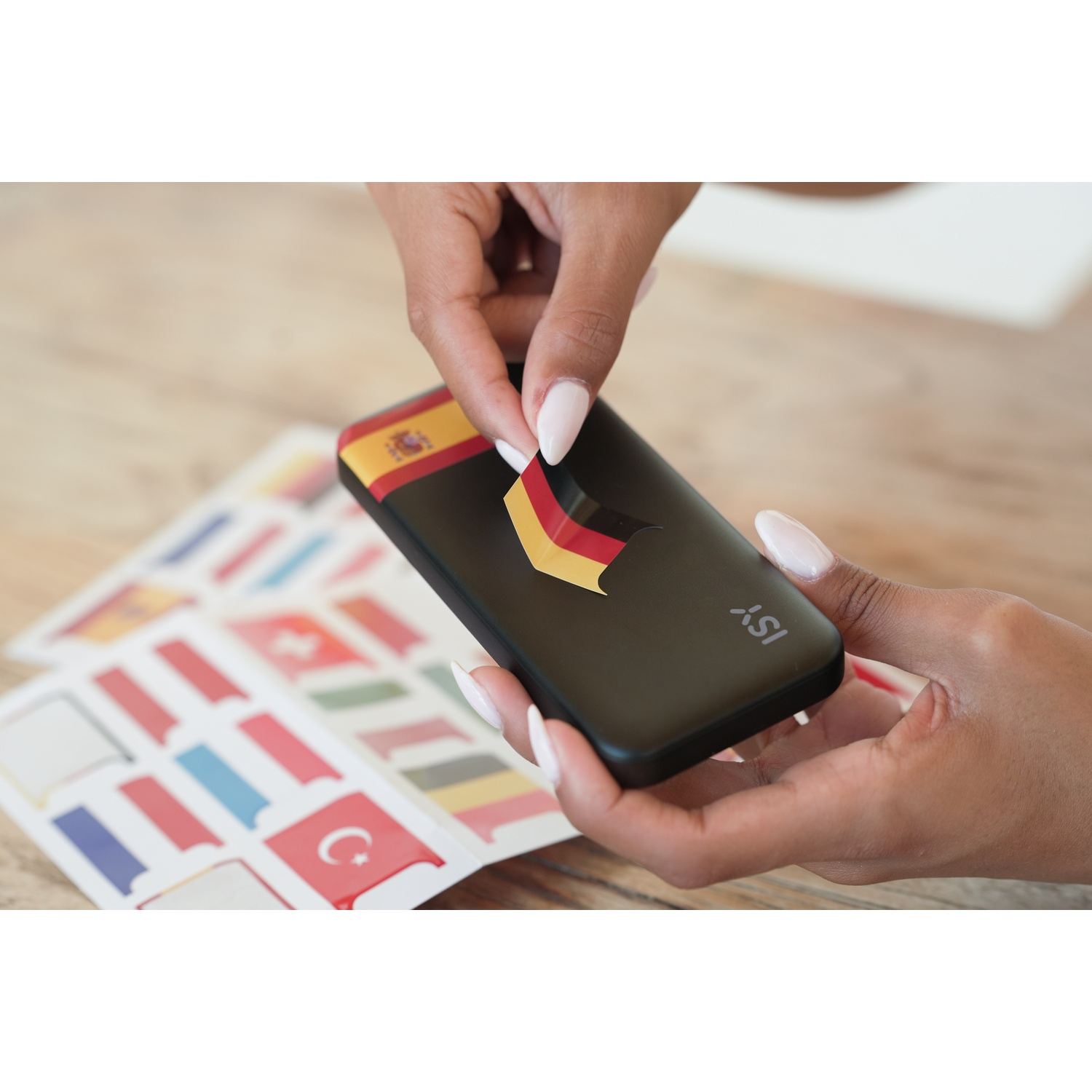 Mani con manicure applicano adesivi con bandiere su uno smartphone nero.