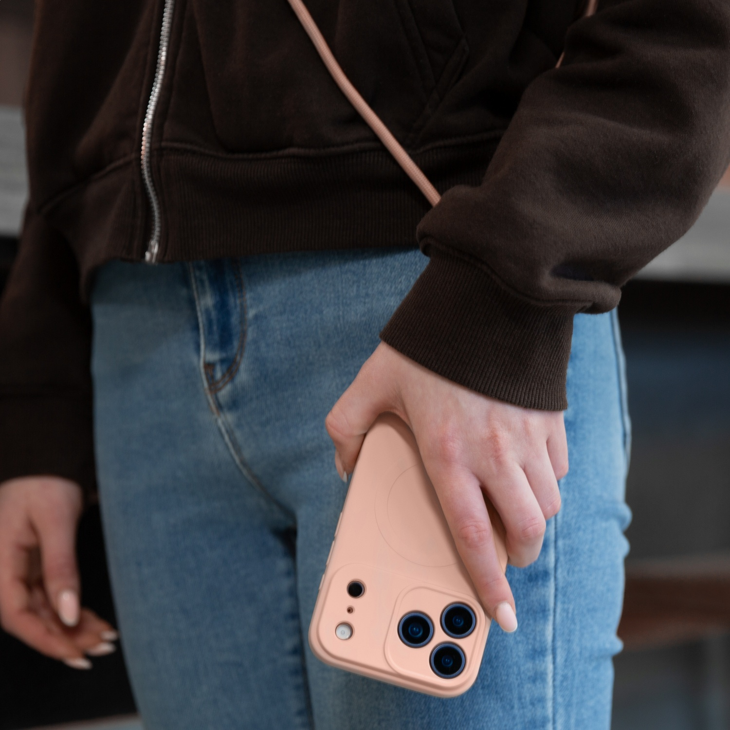 A person in jeans and a brown hoodie holds a light peach-colored phone.
