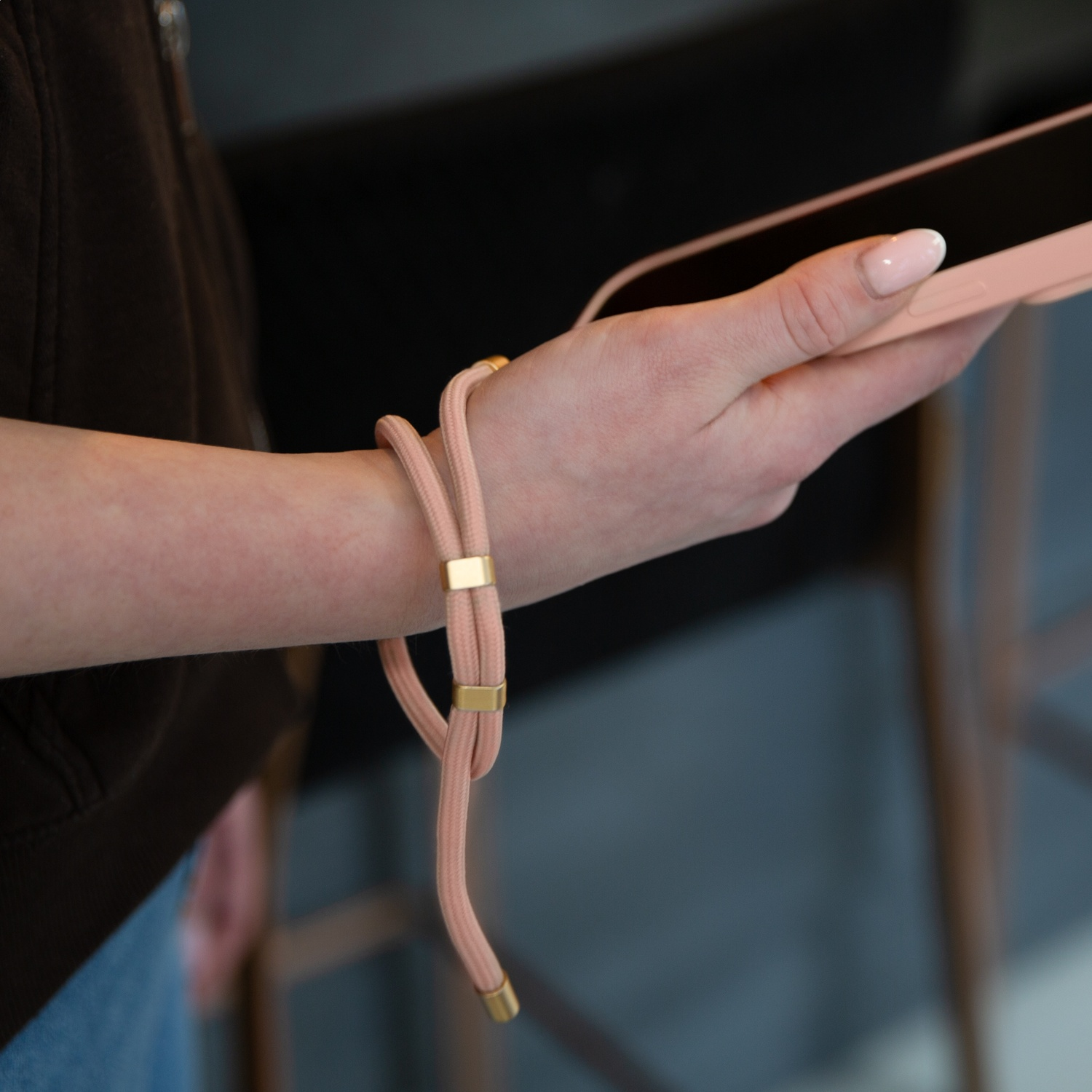 A hand holds a pink smartphone with a wrist strap attached.