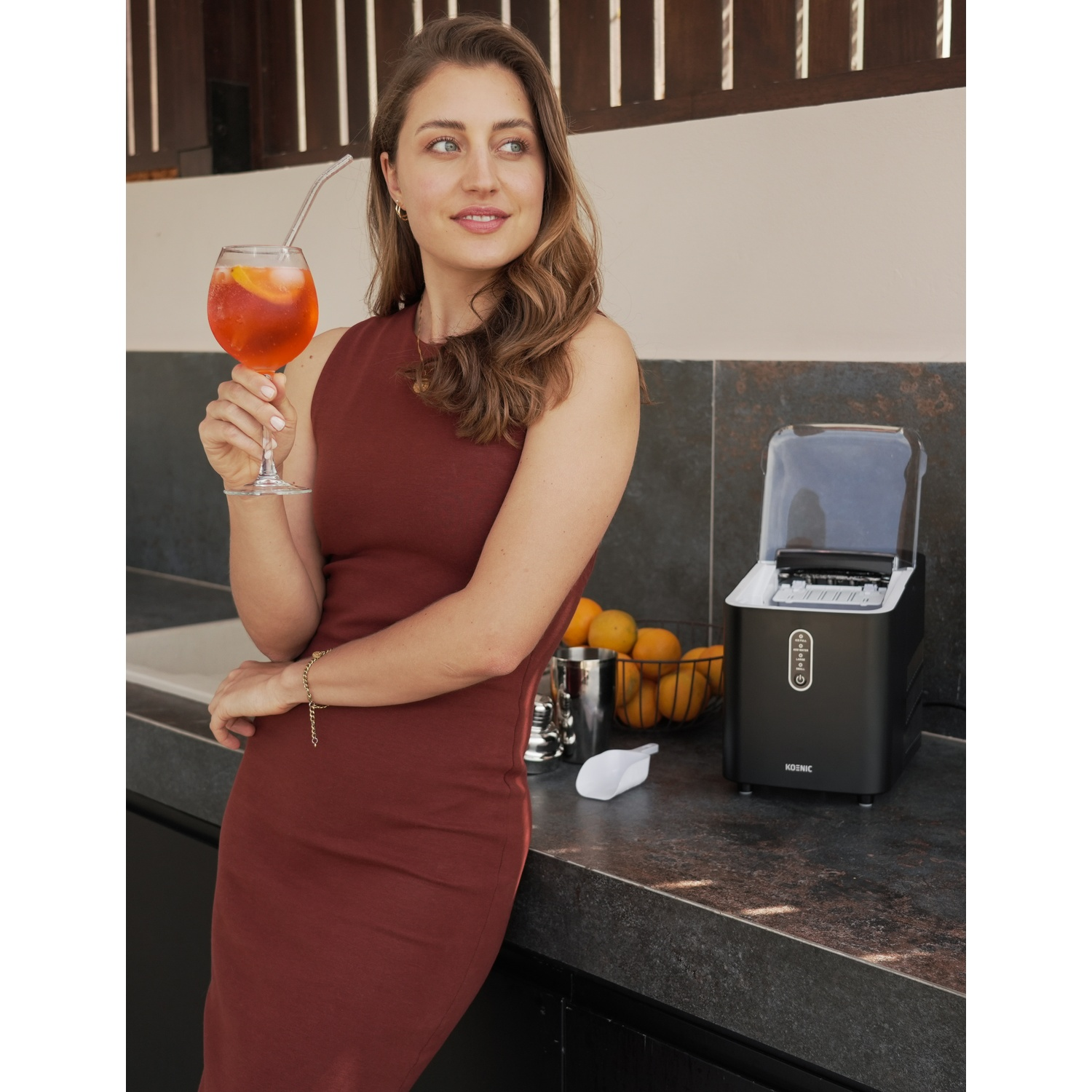 Una donna tiene un cocktail arancione ghiacciato con cannuccia vicino a una macchina del ghiaccio.