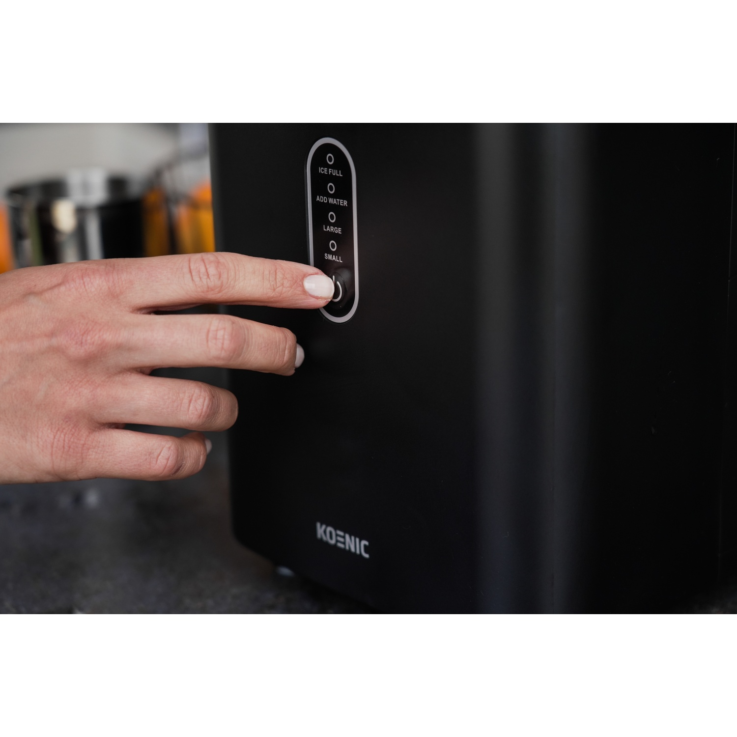 Una mano preme un pulsante su una macchina per il ghiaccio nera con indicatori LED.