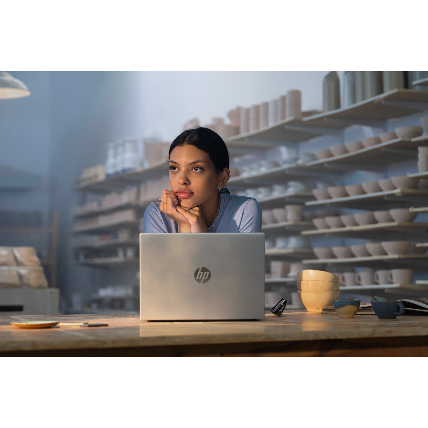 Een vrouw zit aan een houten bureau met een laptop, kijkt peinzend naar rechts.