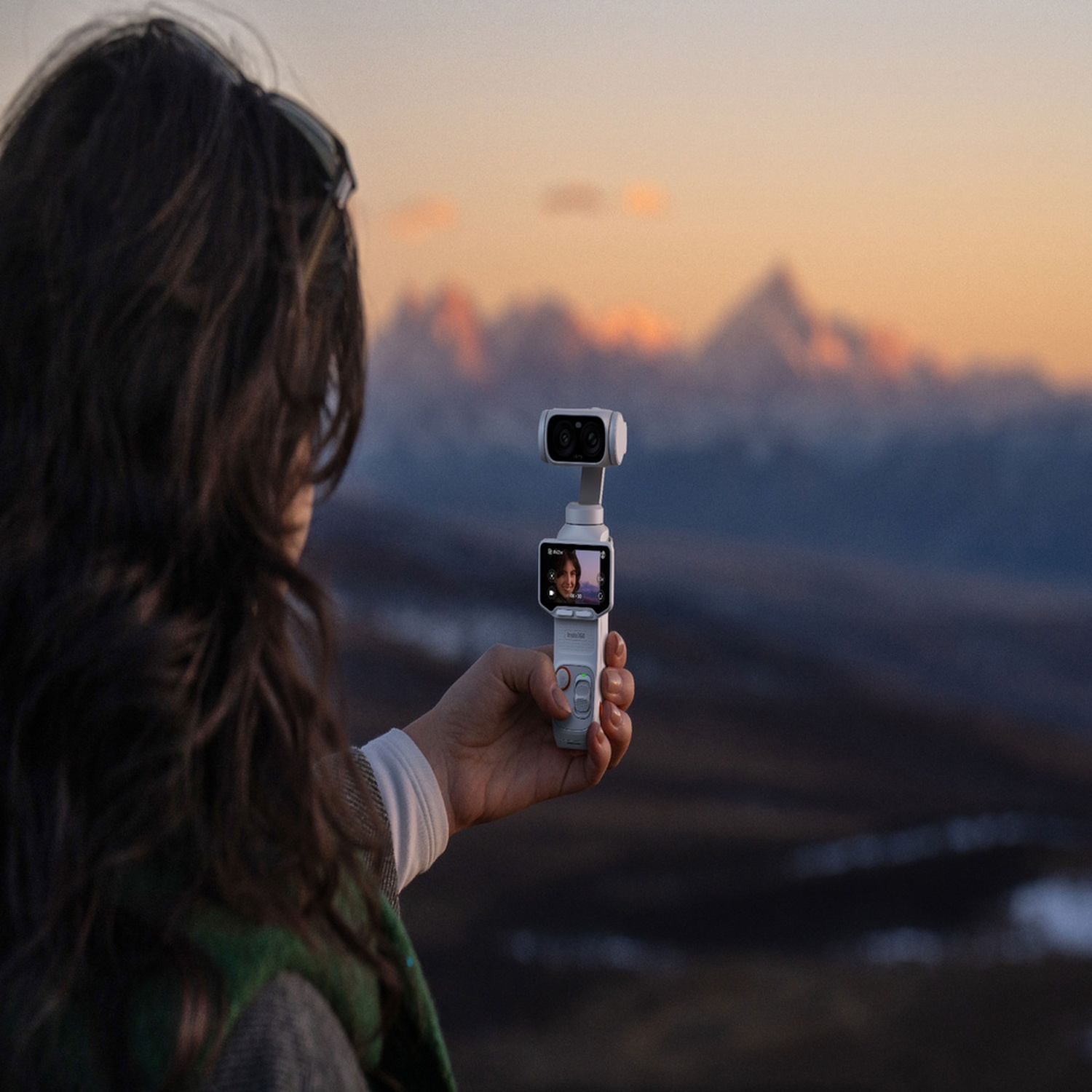 Donna tiene telecamera gimbal con schermo che mostra il suo viso, montagne al tramonto.