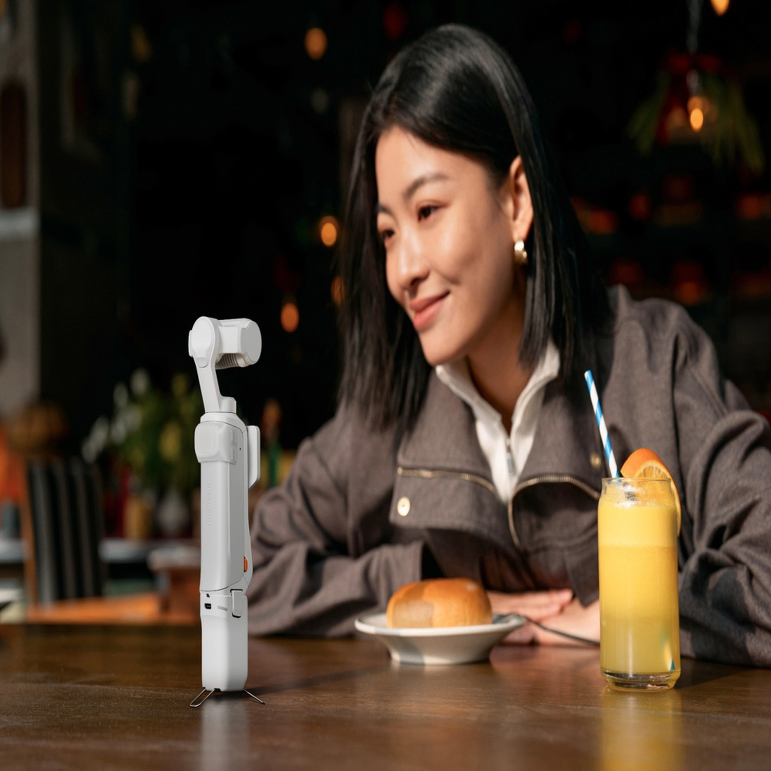 Una donna sorride a un gimbal seduta in un bar. Sul tavolo ci sono una bevanda e un panino.