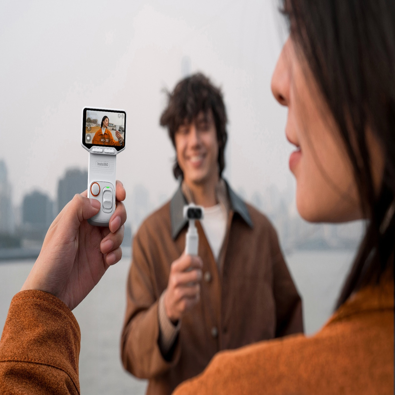 Una mano tiene una fotocamera che mostra un selfie. Un uomo sorride sullo sfondo.