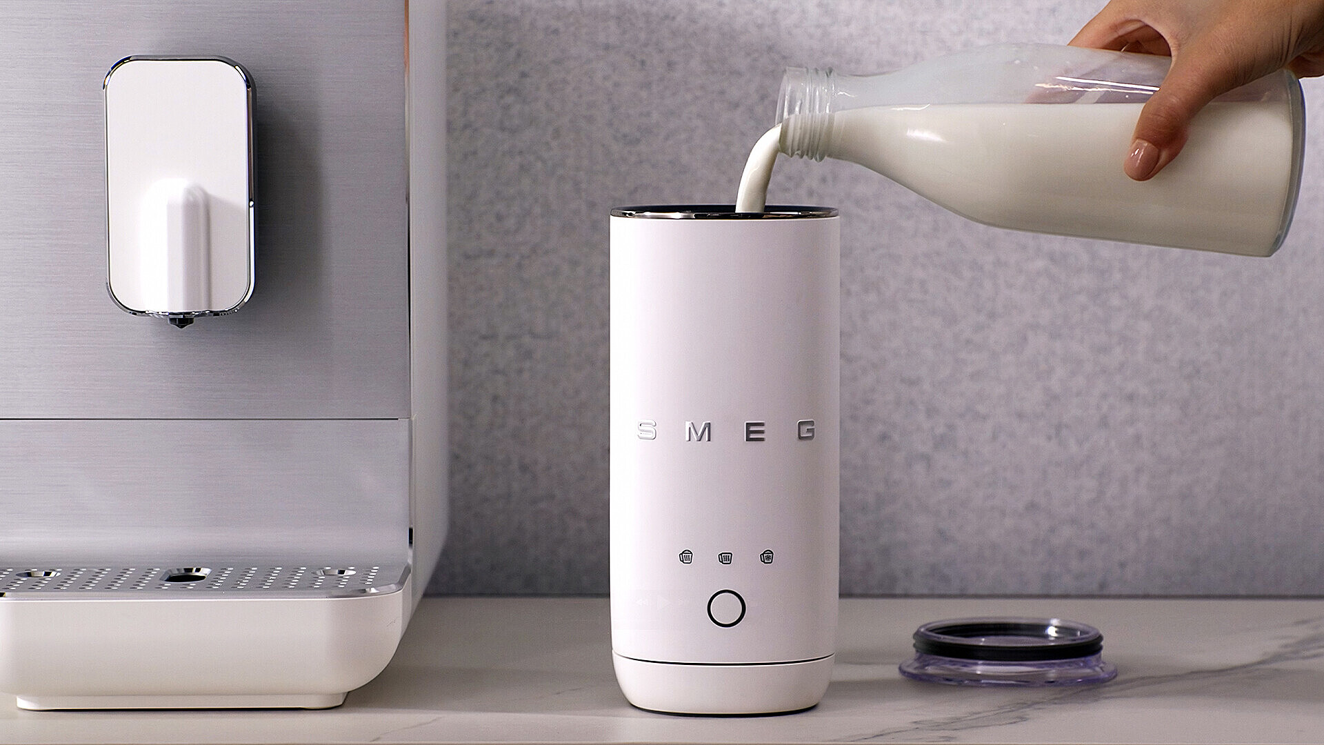 Milch wird aus einer Flasche in einen weißen Milchaufschäumer gegossen.