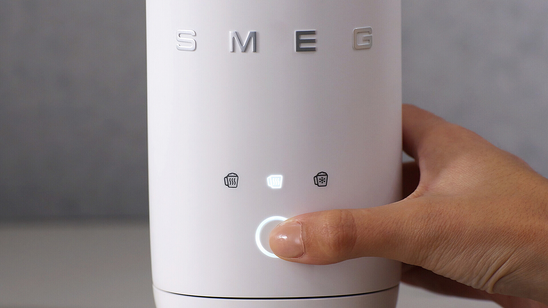 Eine Hand drückt einen beleuchteten Knopf auf einem weißen Smeg-Gerät.