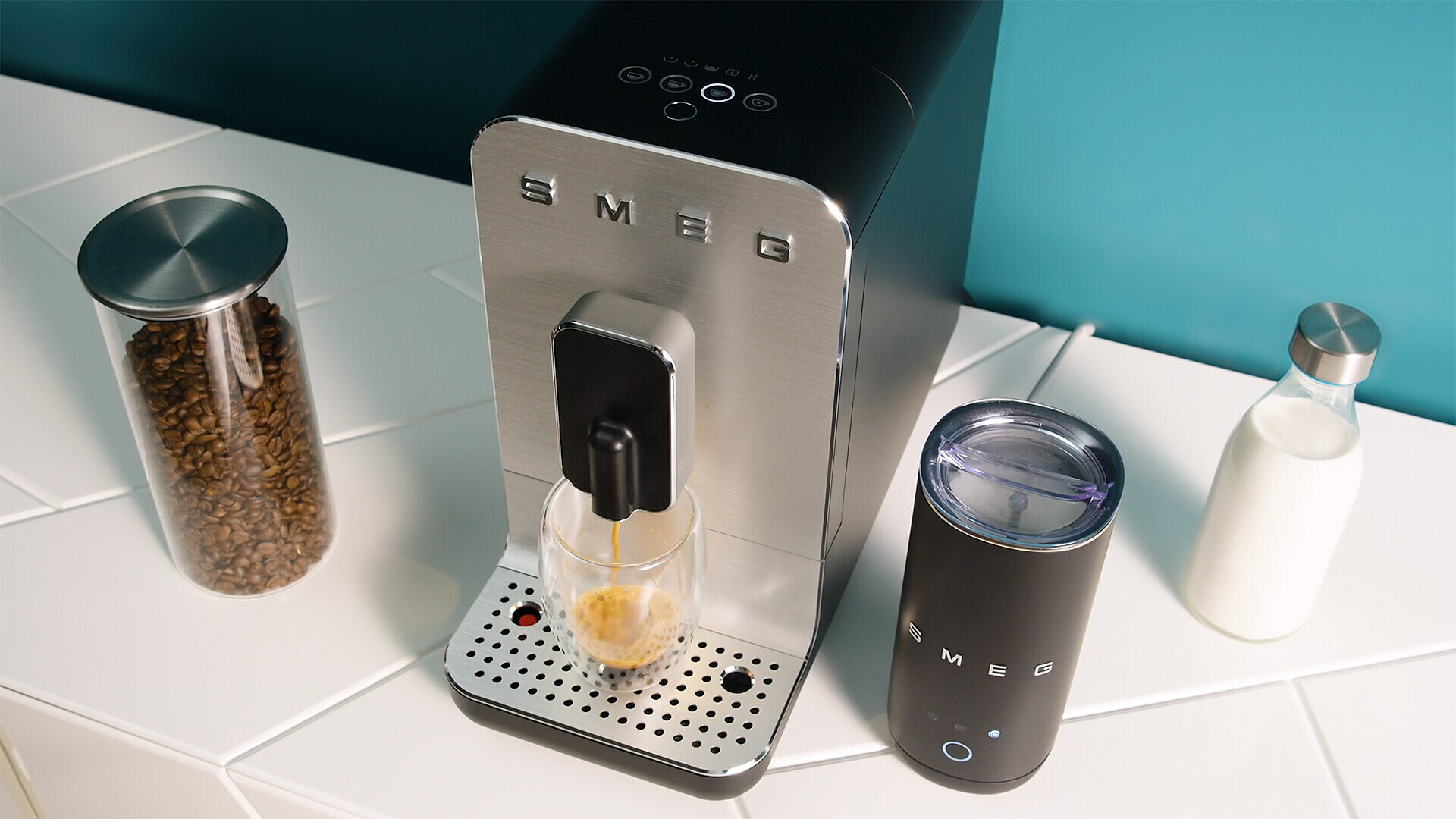 Eine SMEG-Kaffeemaschine brüht Espresso in ein Glas, daneben Kaffeebohnen und Milch.