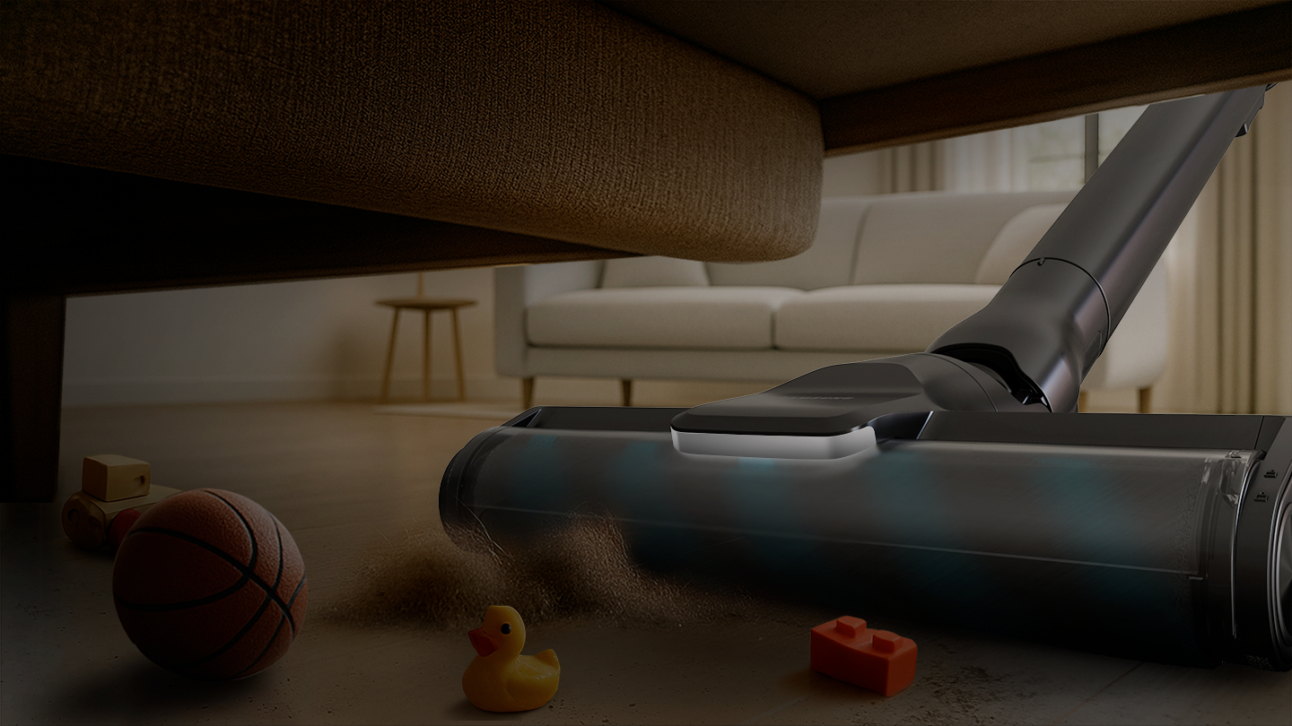 Staubsauger reinigt unter einem Sofa; Spielzeug auf dem Boden.
