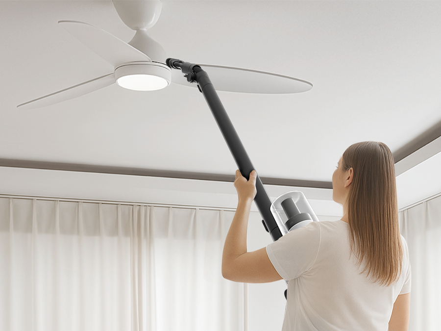 Eine Frau saugt einen Deckenventilator mit einer Handstaubsaugerstange ab.