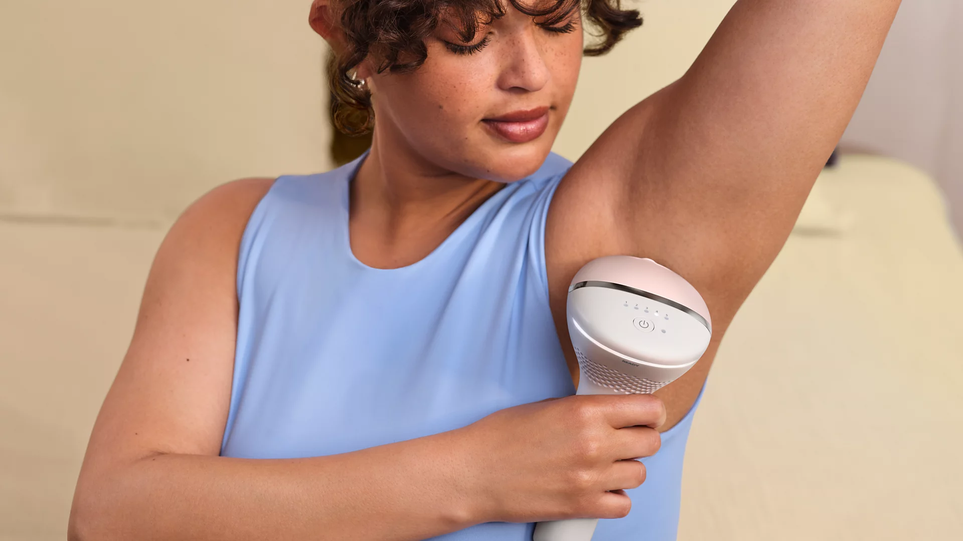 Femme en haut bleu utilise un appareil d'épilation IPL sur l'aisselle.