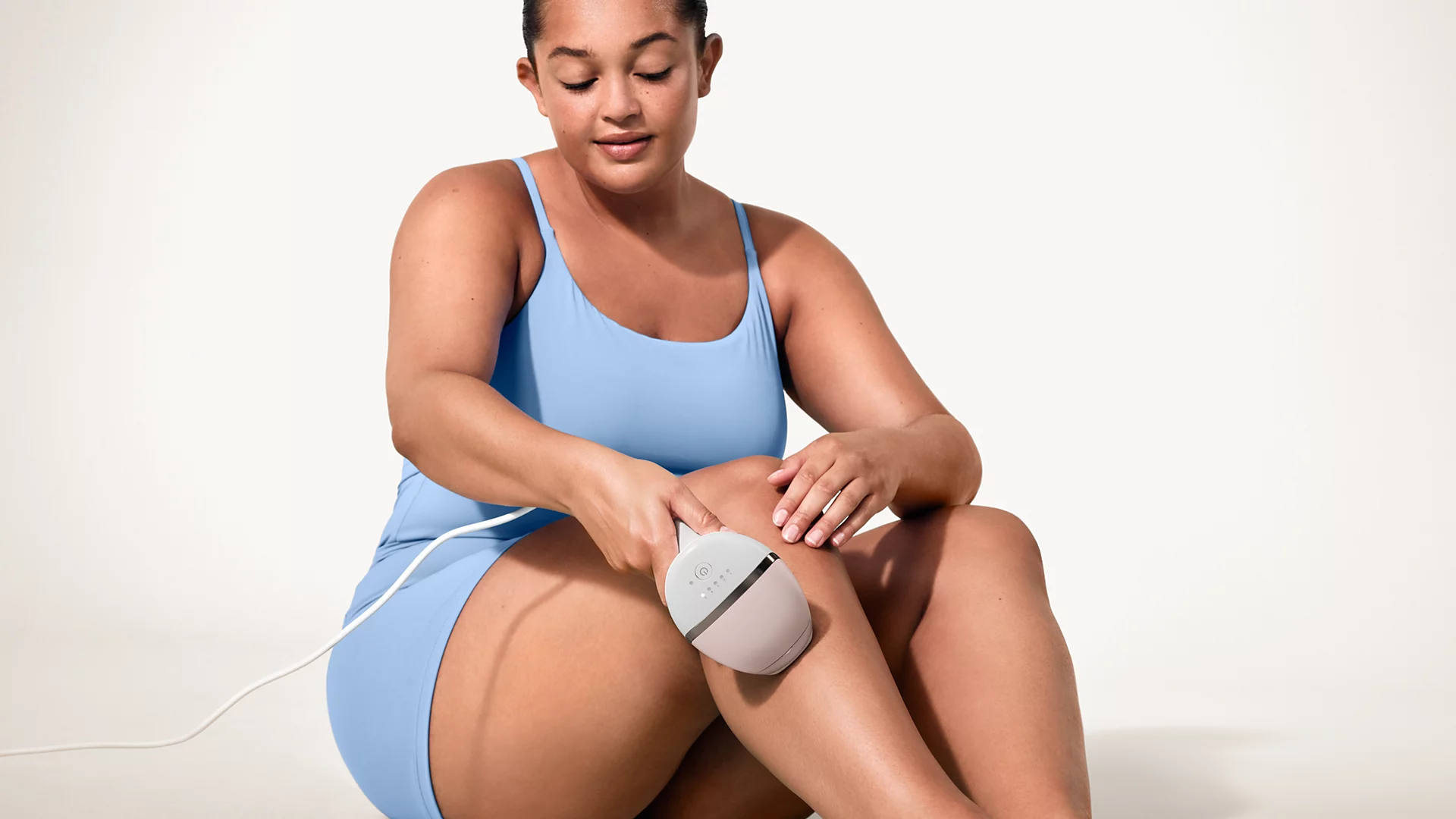 Une femme en maillot de bain bleu clair utilise un appareil d'épilation sur sa jambe.