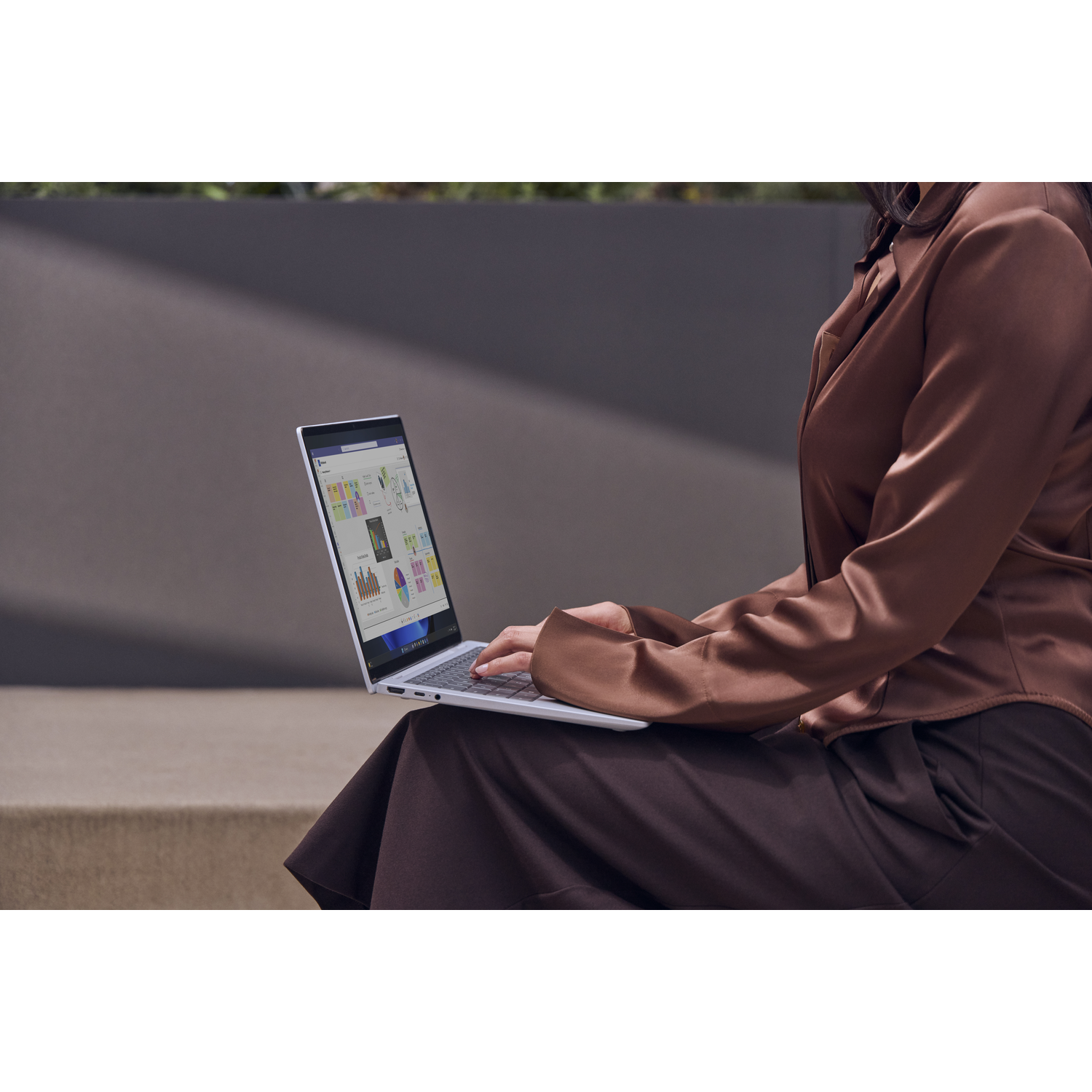 Vrouw in bruine outfit typt op laptop met grafieken, buiten zittend.