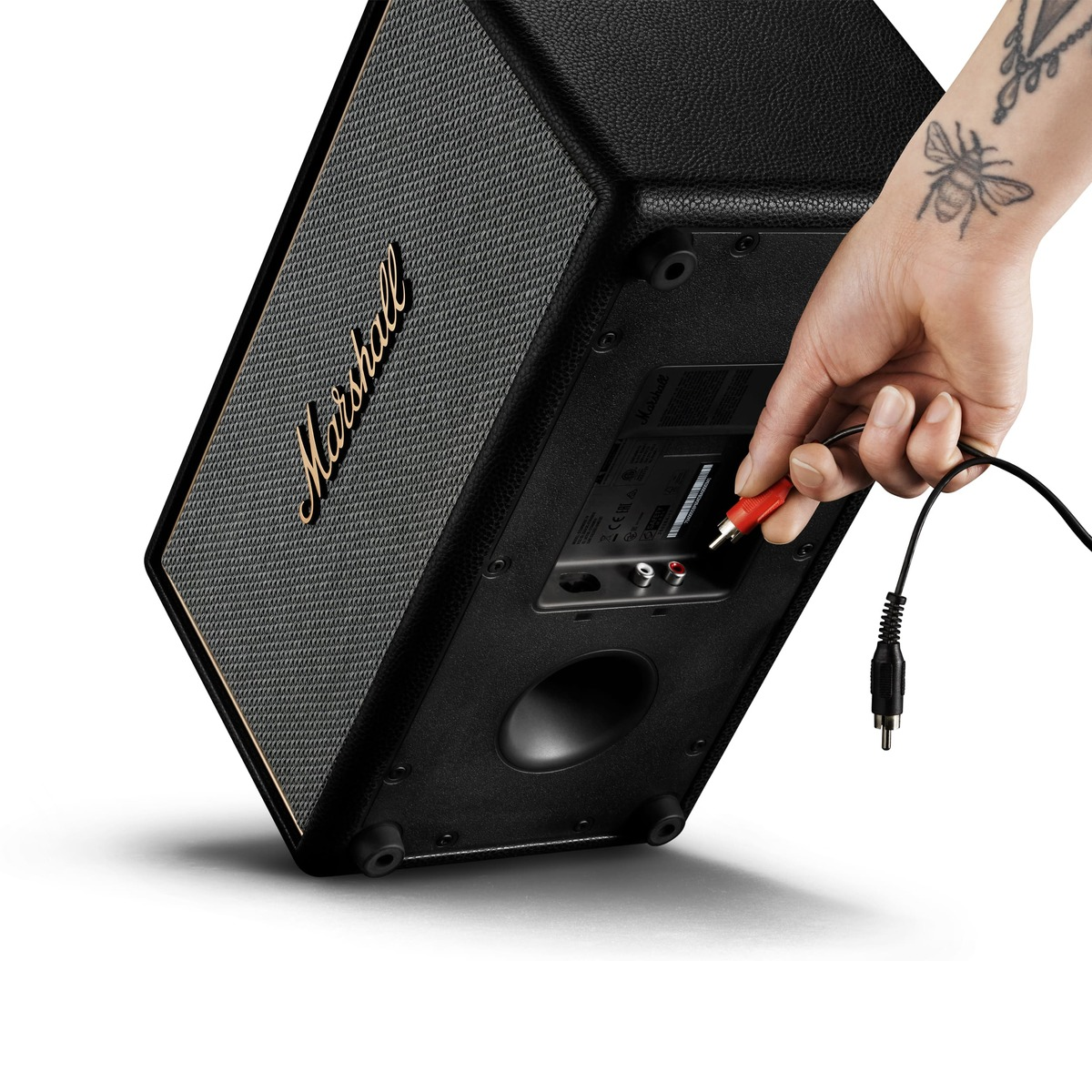 Hand mit Bienen-Tattoo steckt roten Audiostecker in schwarzen Marshall Lautsprecher.