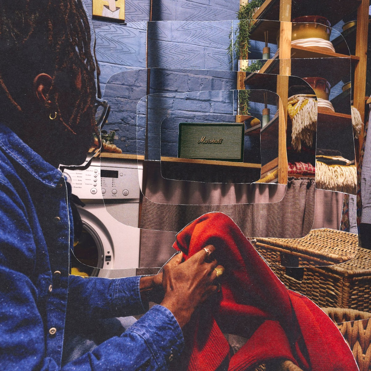 Ein Mann mit Dreadlocks im blauen Hemd faltet rote Kleidung neben einer Waschmaschine.