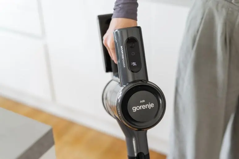 Egy kéz sötét porszívót fog, Gorenje logóval.