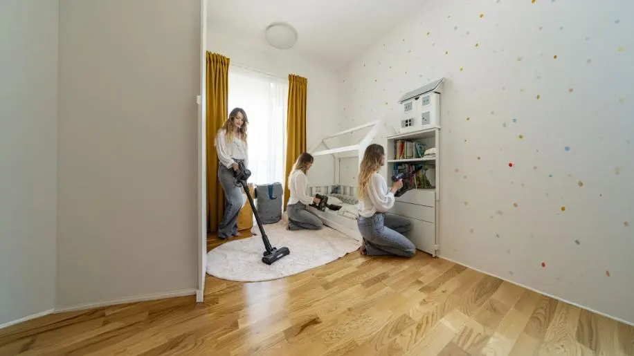 Egy nő porszívóval takarít egy gyerekszobában és rendet rak.