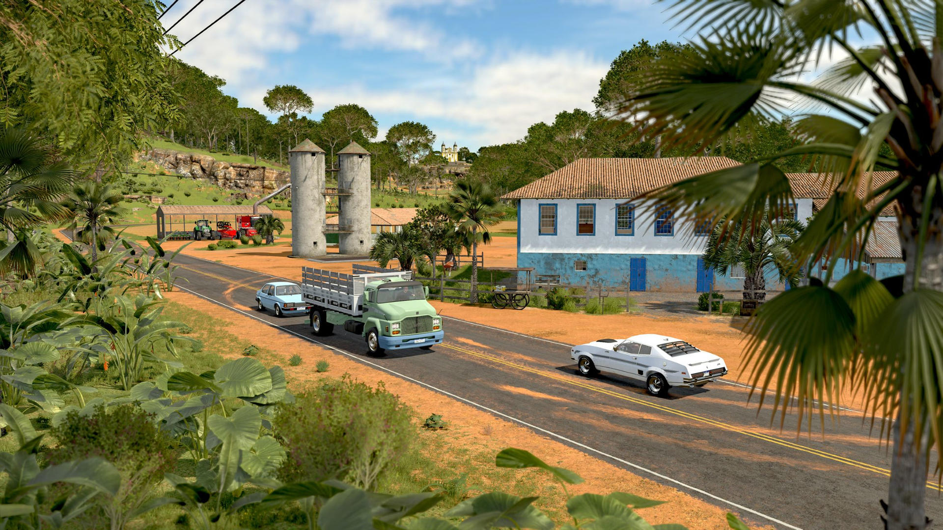 Grüner LKW, weißes und blaues Auto auf Straße bei Bauernhof mit Silos und blauem Haus.