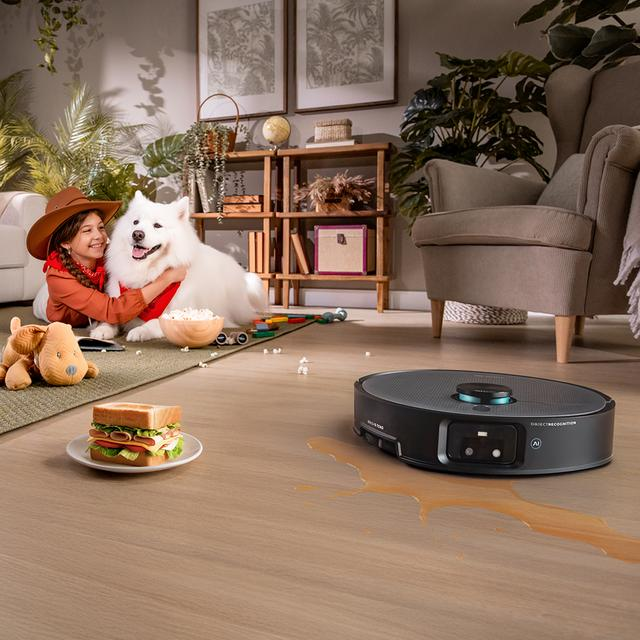 Kız beyaz köpeği kucaklıyor. Robot süpürge dökülen sıvıyı temizliyor. Sandviç ve patlamış mısır yakında.
