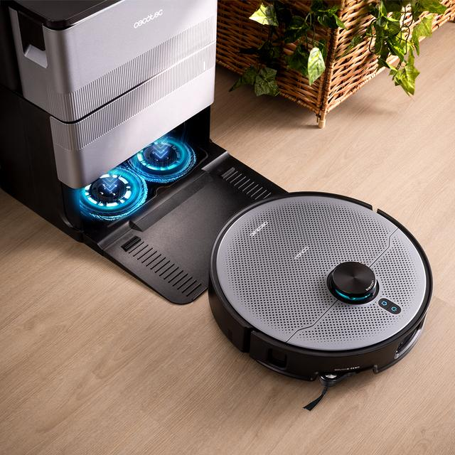 Mavi ışıklı şarj istasyonunda robot süpürge. Arkada bitkili hasır sepet.