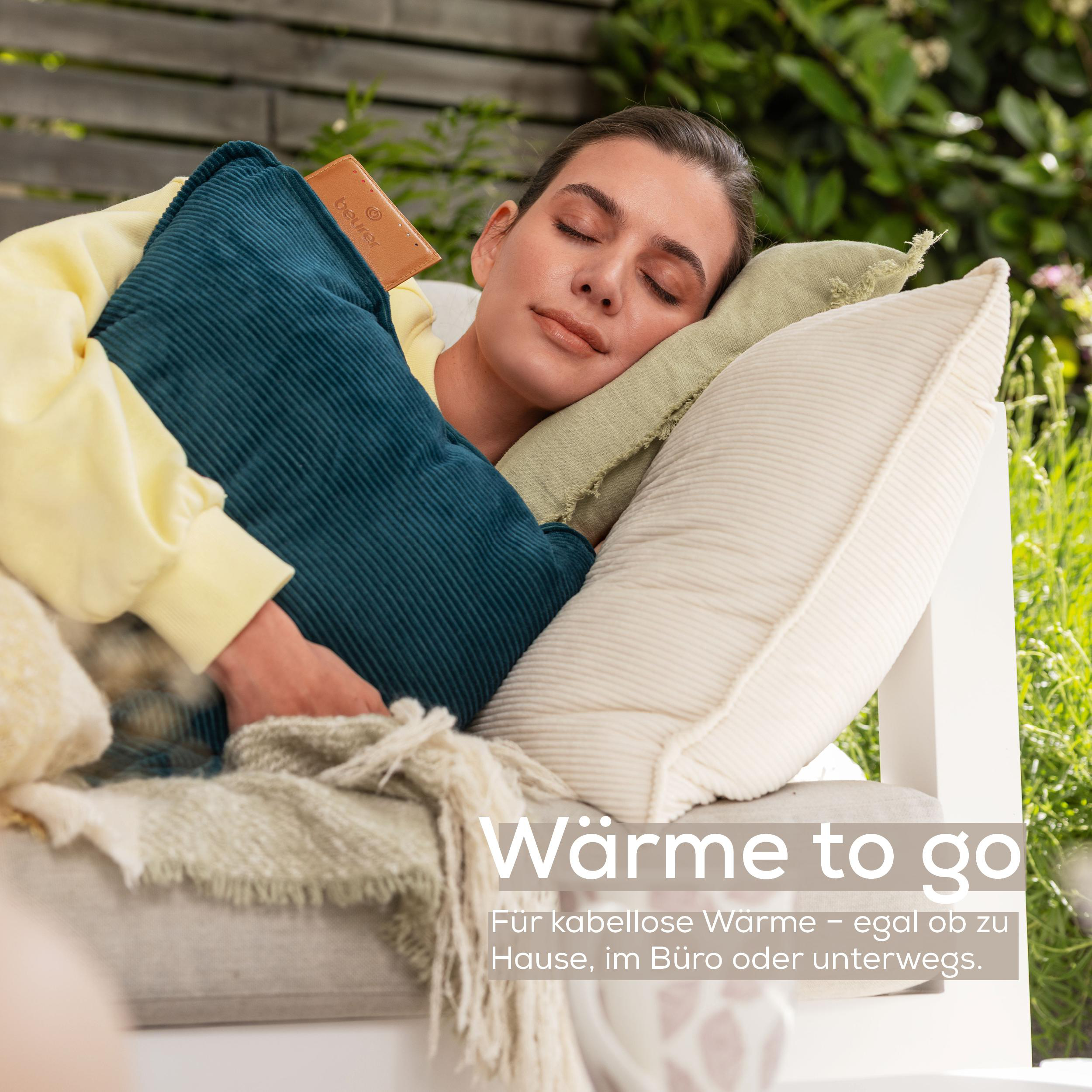 Eine Frau schläft auf einem Sofa im Freien, umgeben von Kissen und Decken.