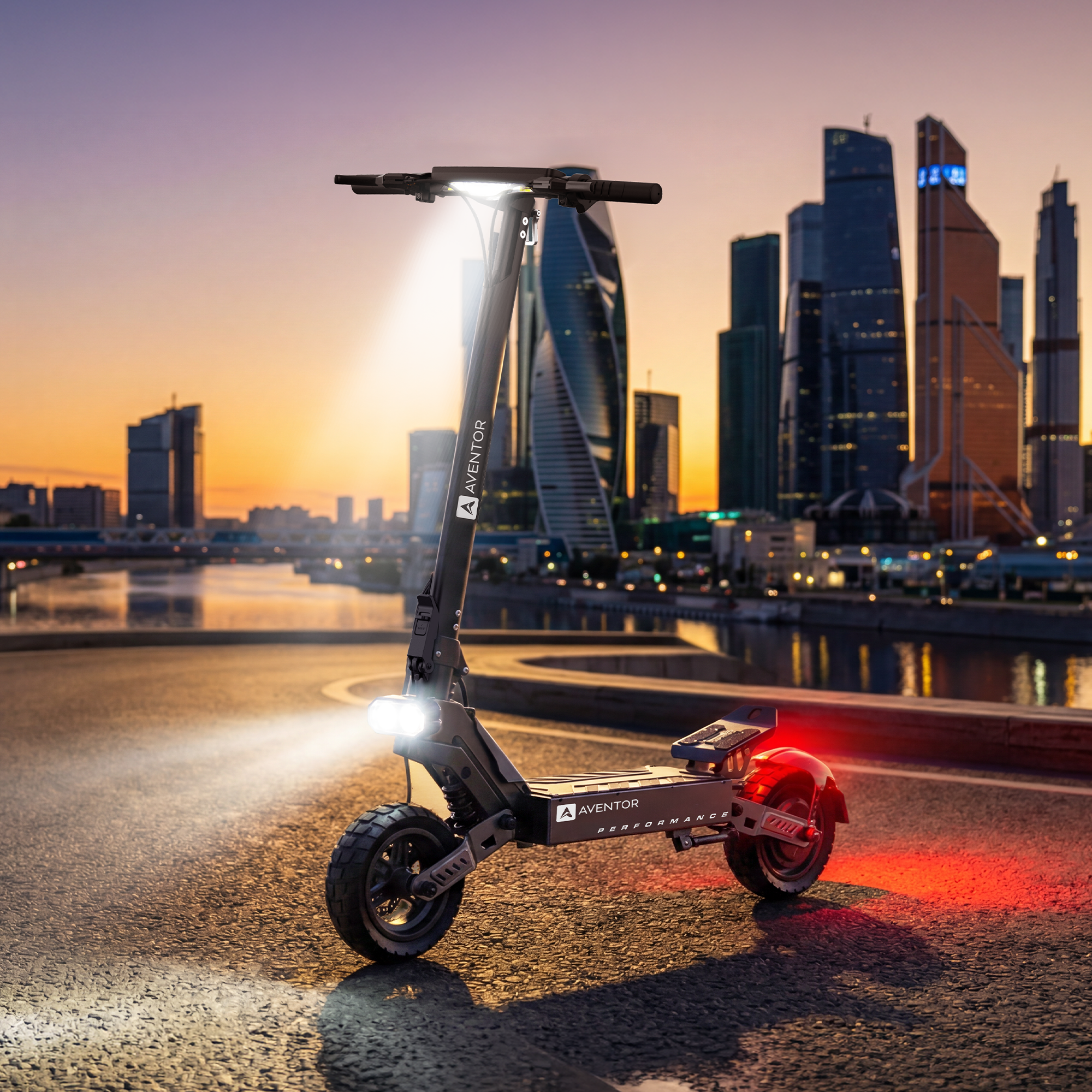 Gün batımında şehir silüeti önünde ışıkları yanan siyah elektrikli scooter.
