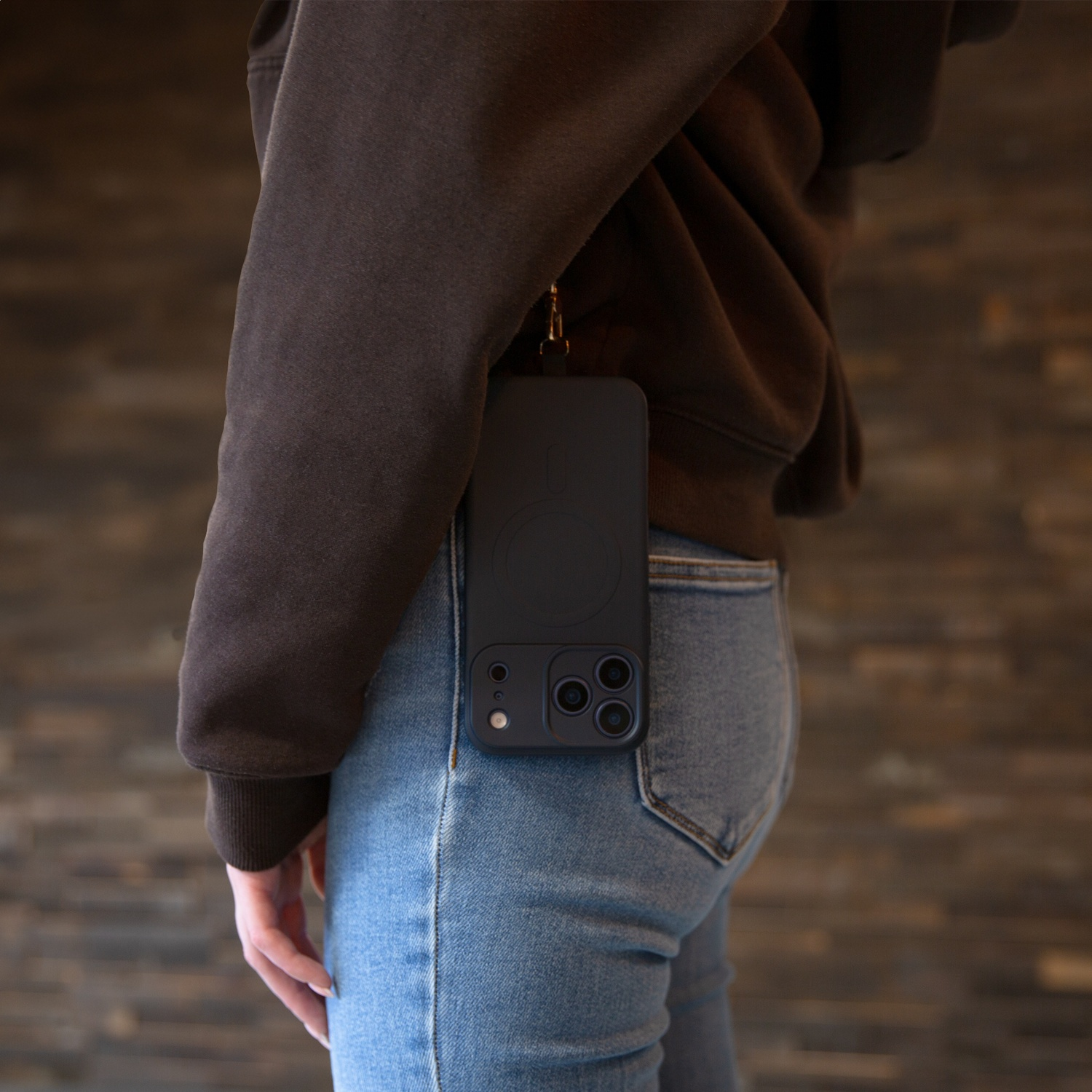 Black phone on lanyard attached to brown hoodie and blue jeans.