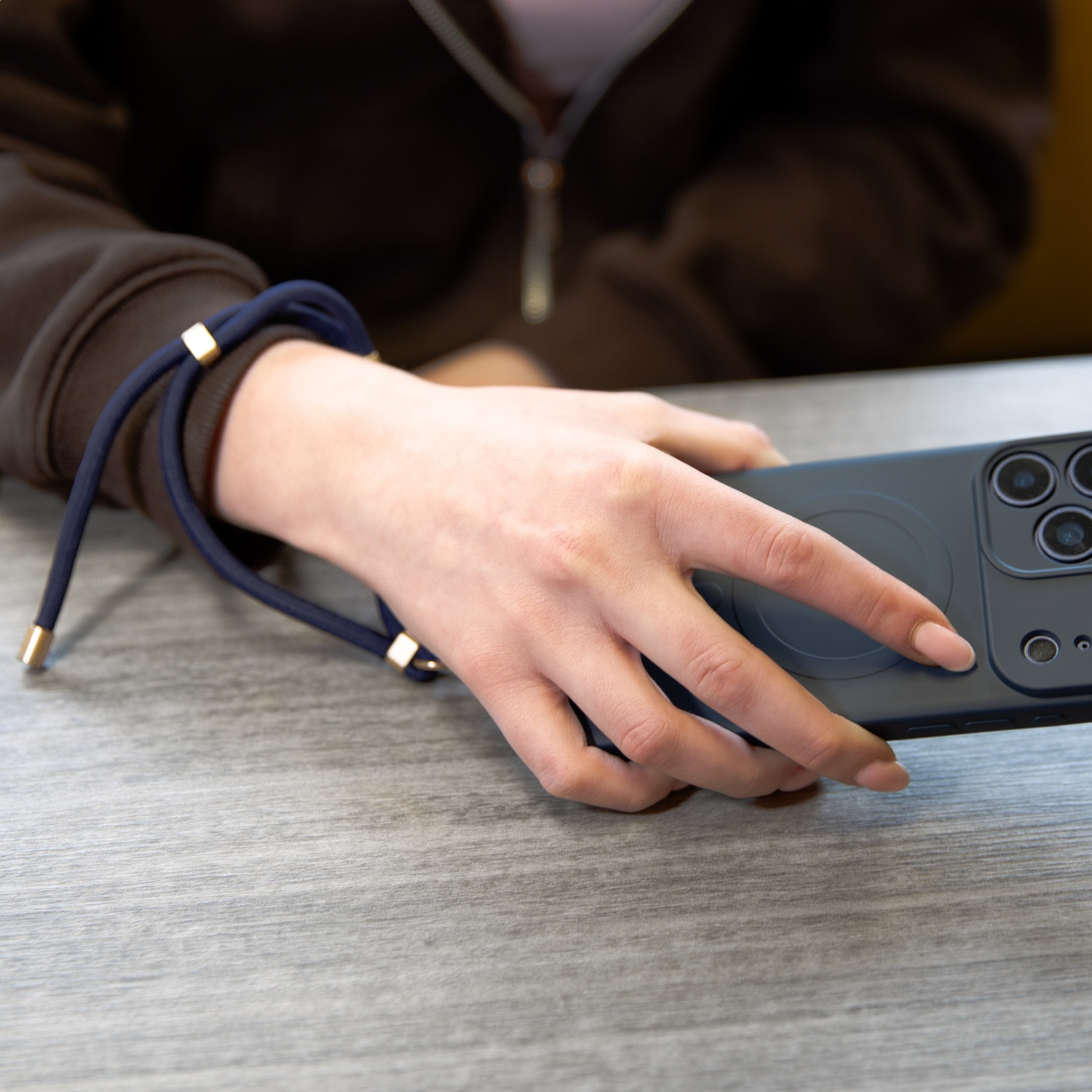 A hand holds a smartphone with a blue wrist strap and gold accents.