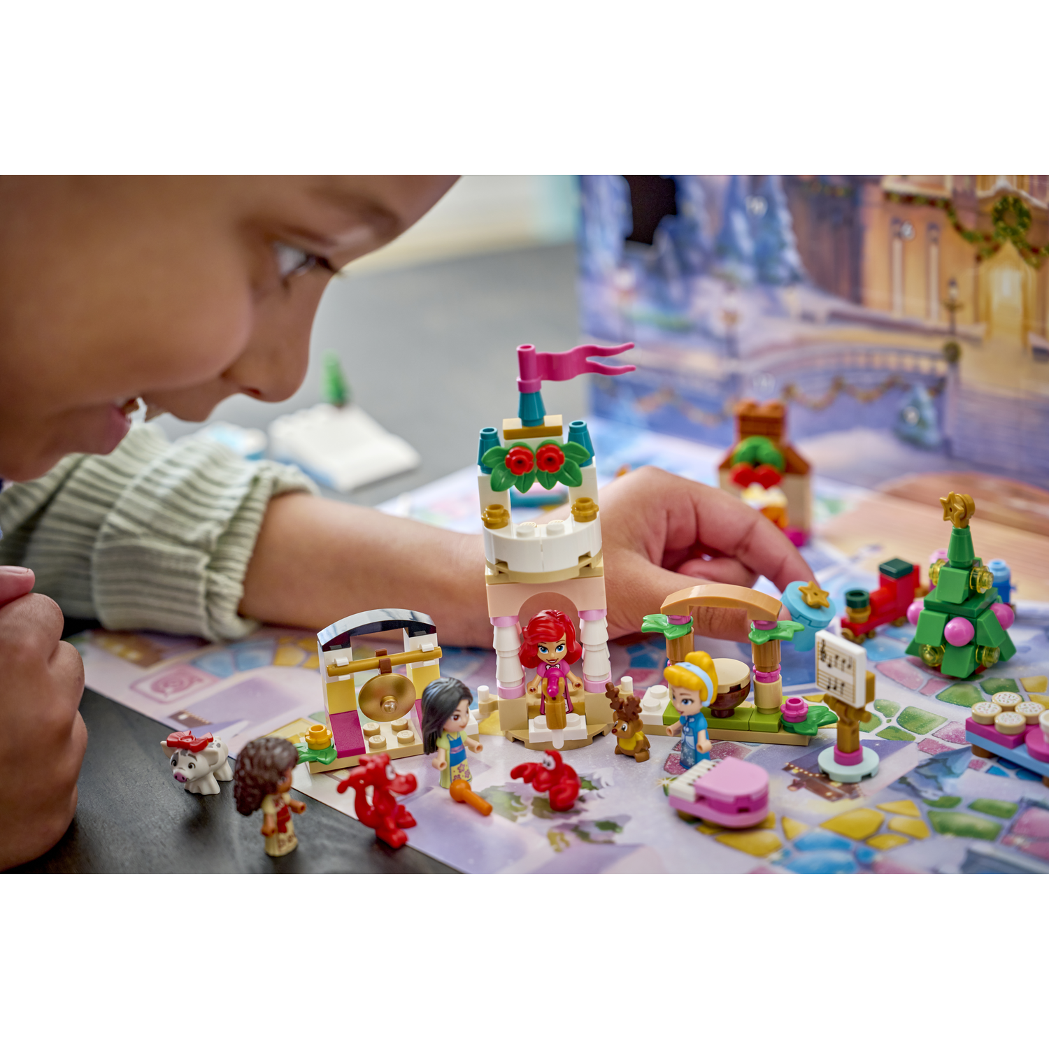 Un enfant joue avec une scène de calendrier de l'Avent LEGO avec des figurines, une tour, un sapin de Noël et un renne.