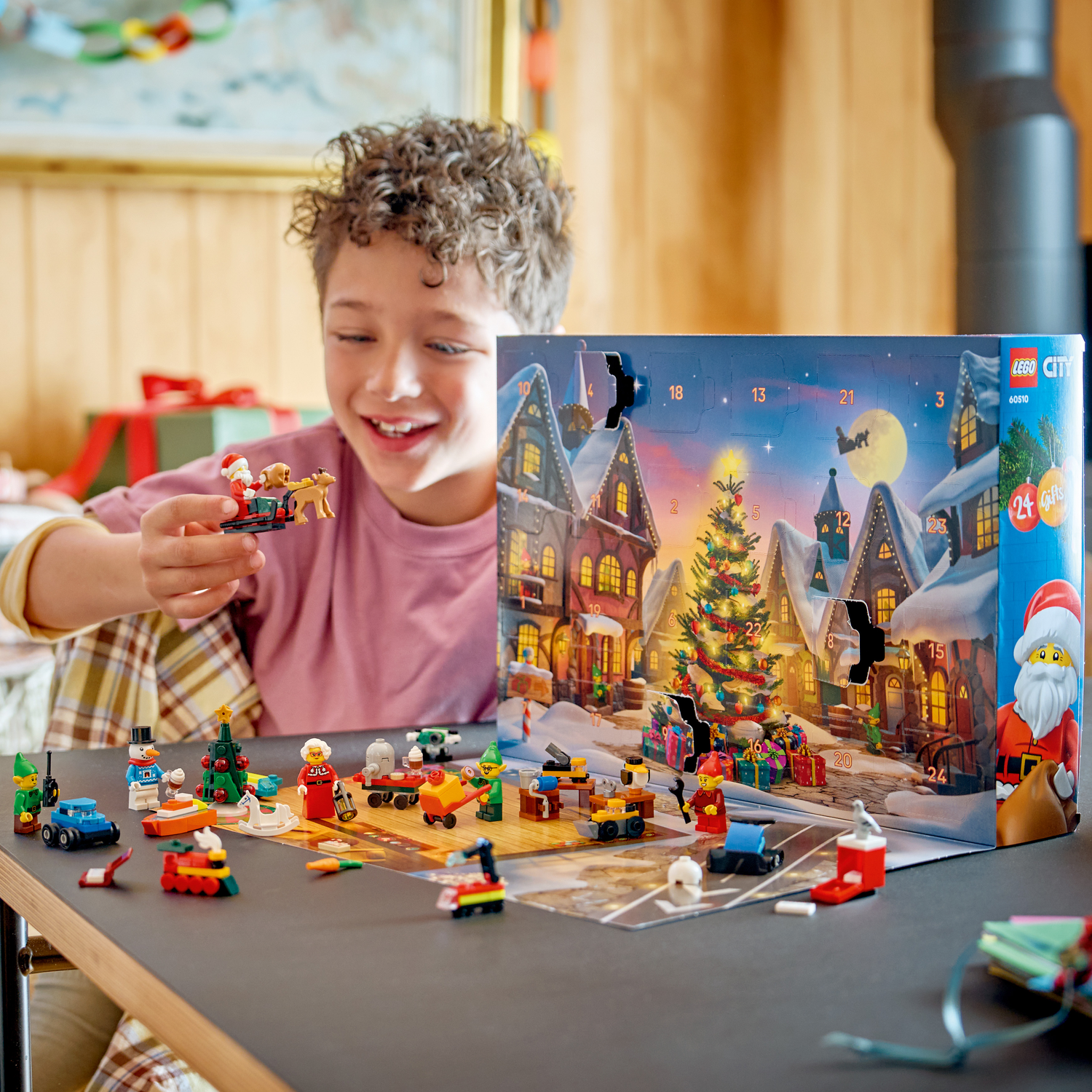 Een jongen opent een LEGO City adventskalender met kersttaferelen en figuren.