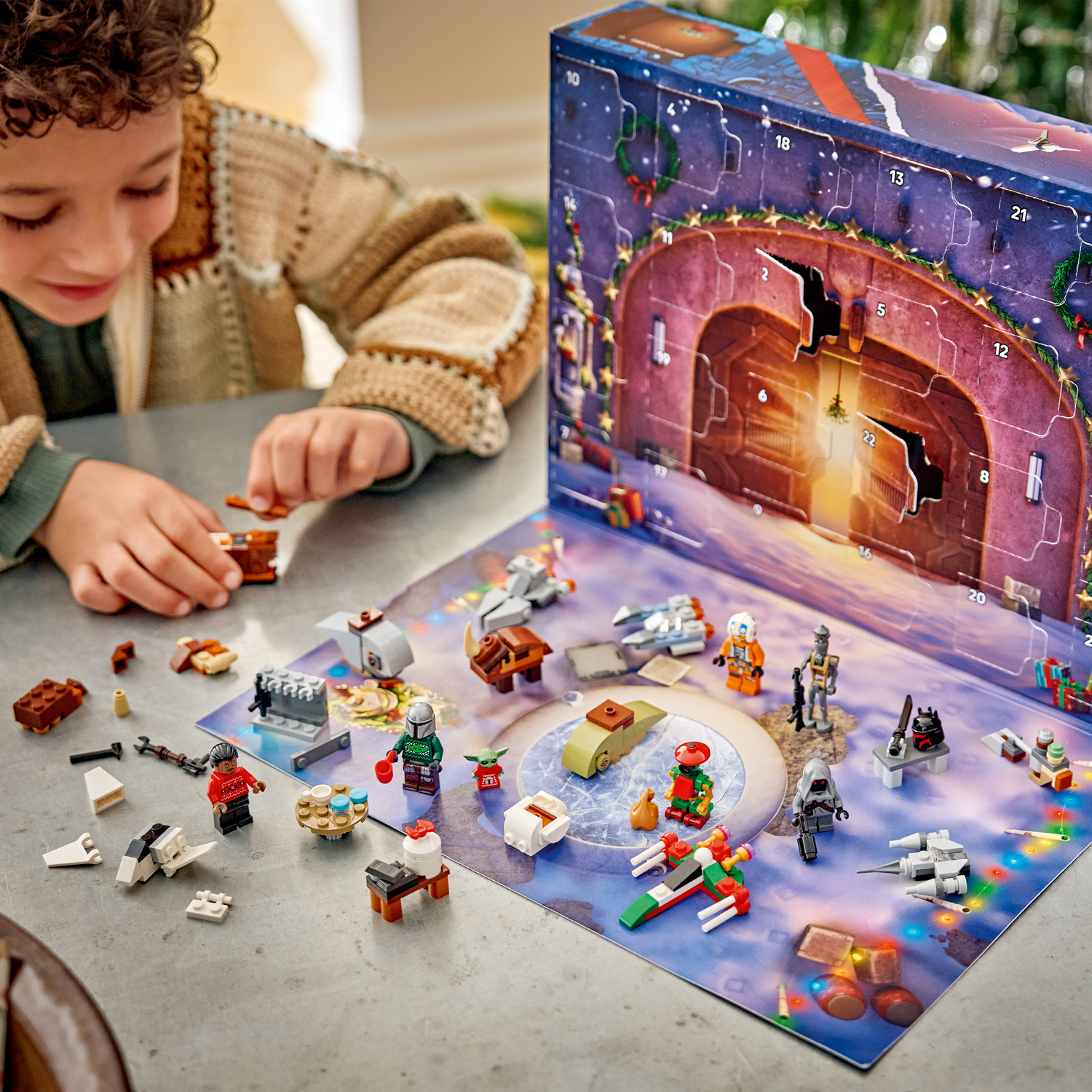 Un garçon joue avec des figurines et véhicules Lego d'un calendrier de l'Avent Star Wars.
