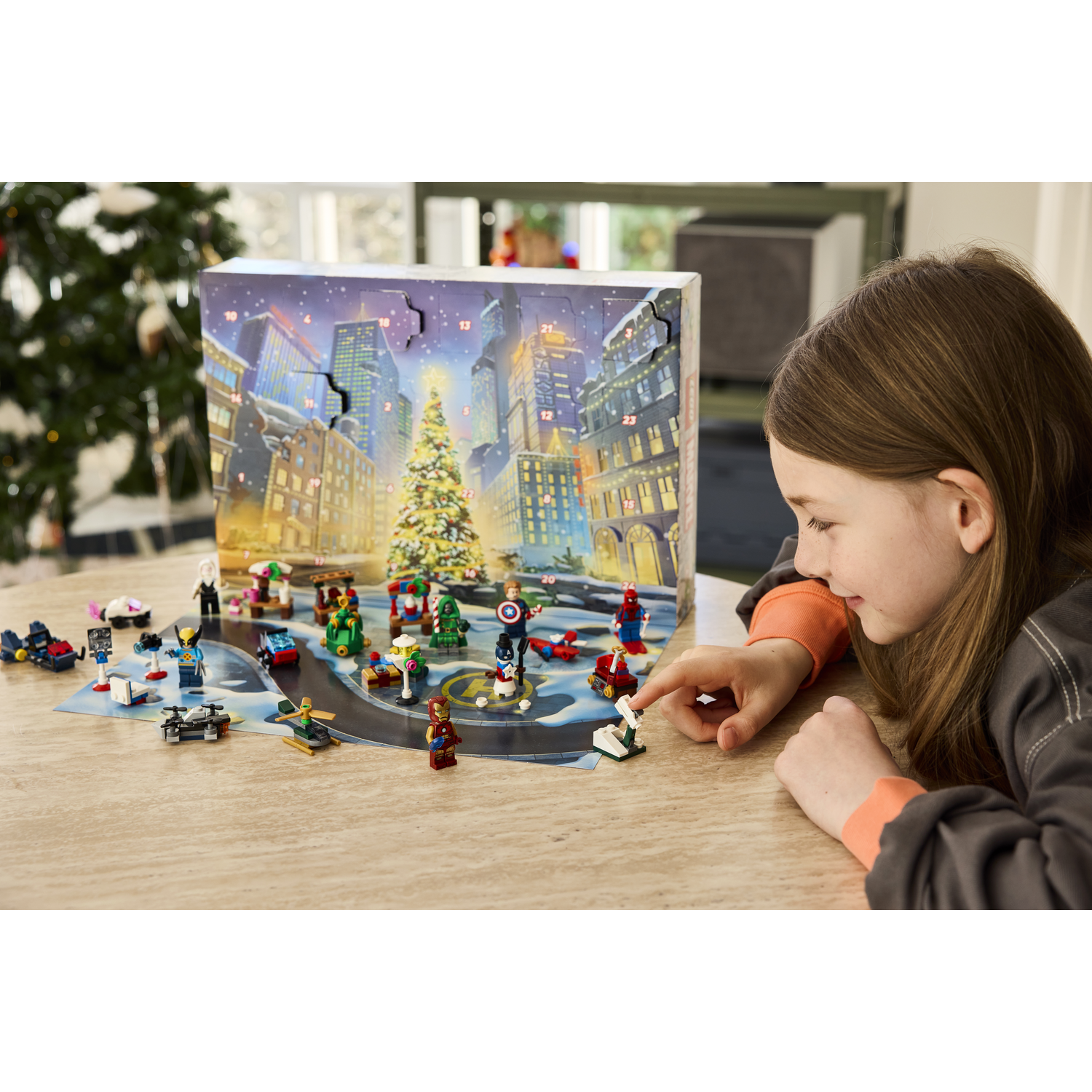 Une fille ouvre un calendrier de l'avent avec des figurines et véhicules de super-héros.