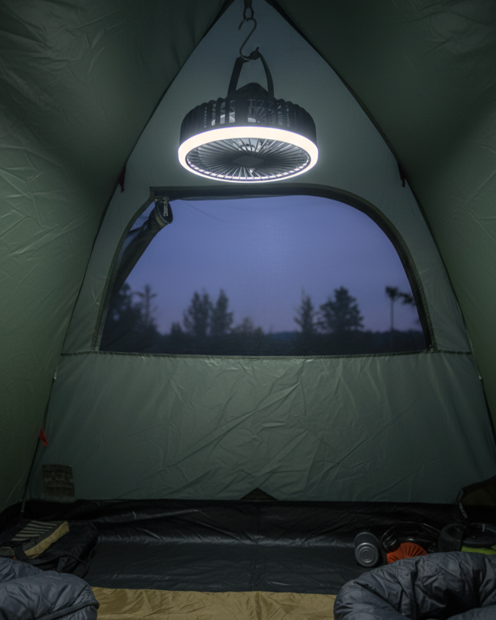 Egy világítós kemping ventilátor lóg egy sátorban. Kint szürkület van.