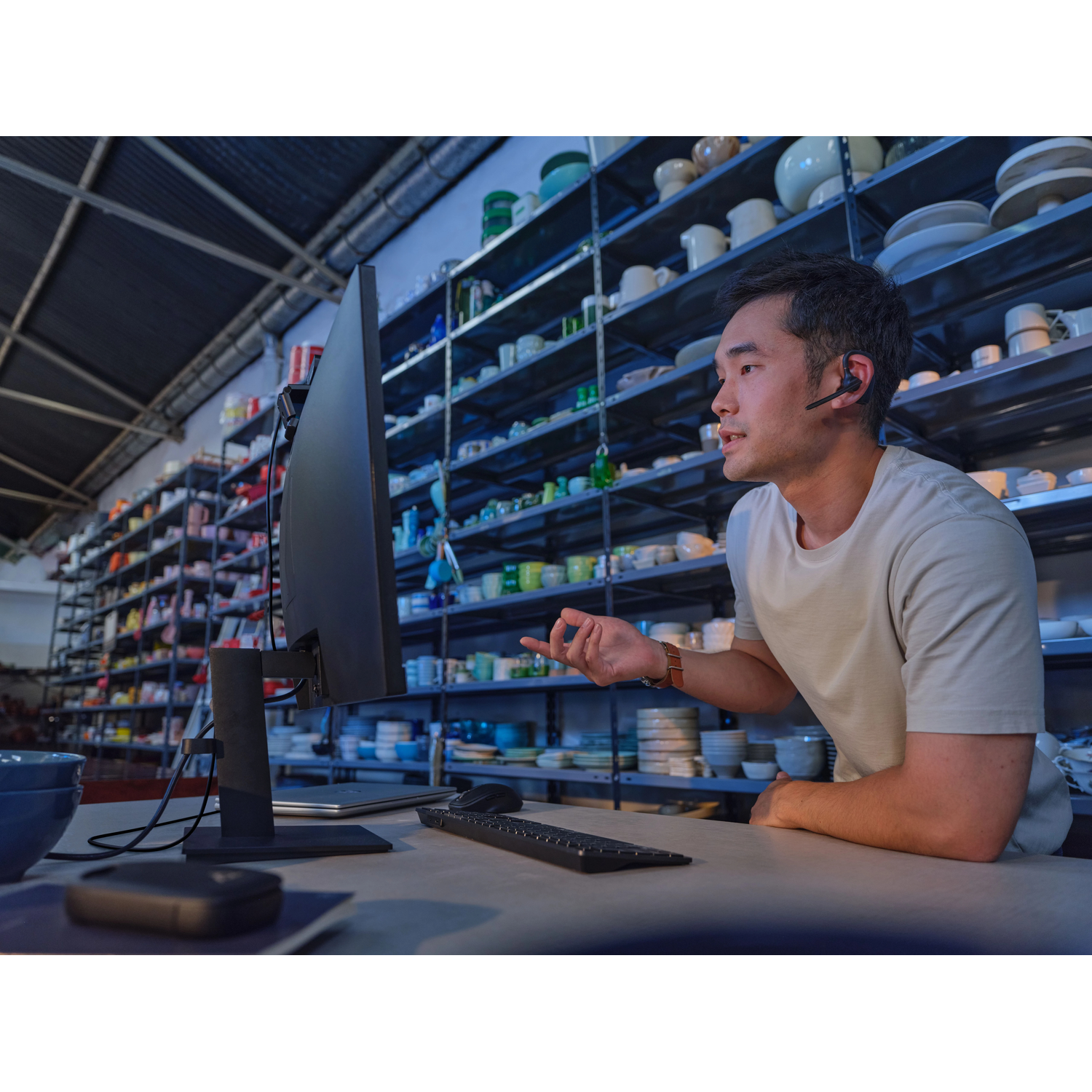 Man in een magazijn, met headset, praat tegen een computerscherm.